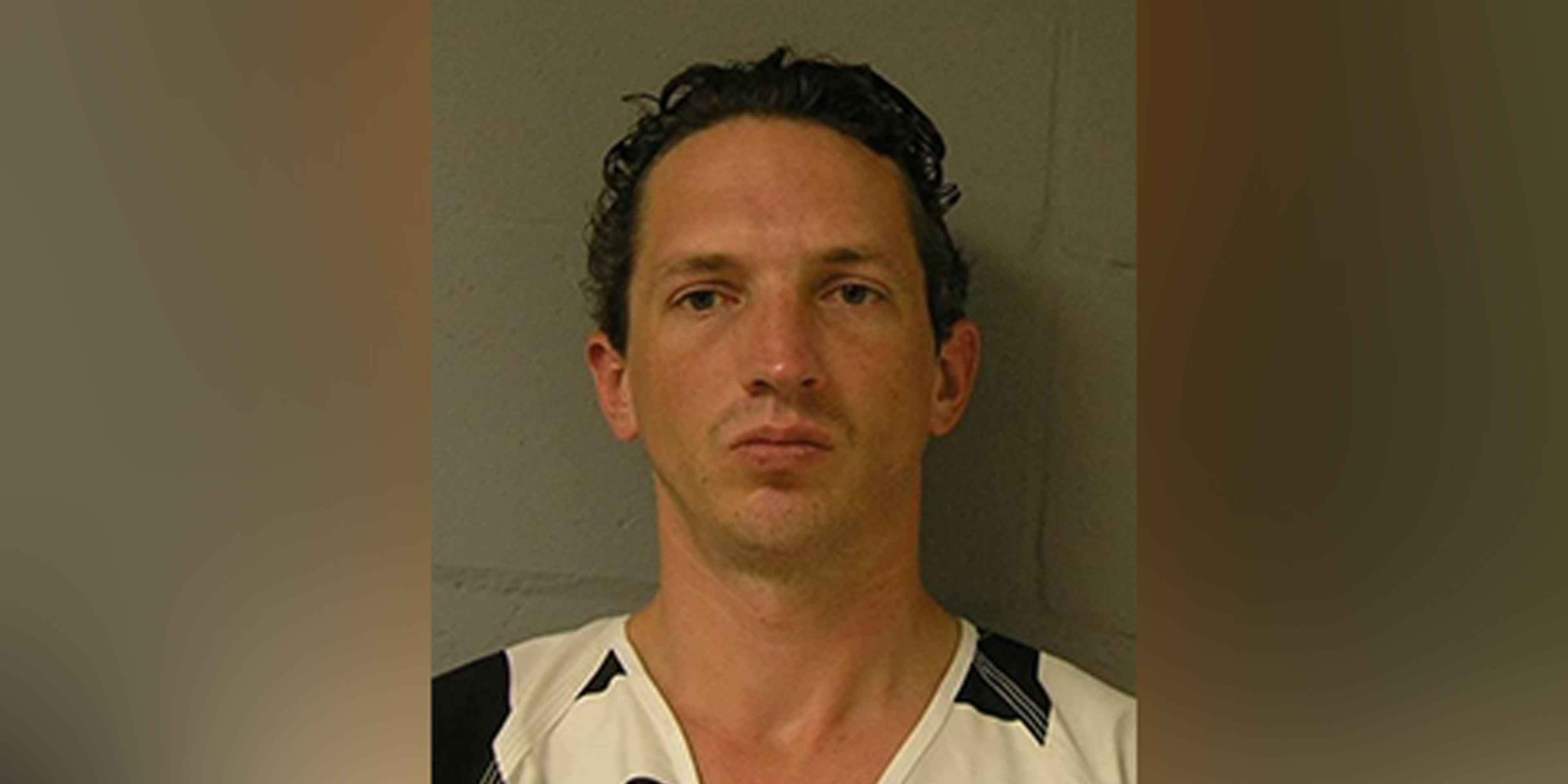 The image shows a close-up portrait of a man with dark hair and a serious expression, set against a plain background.