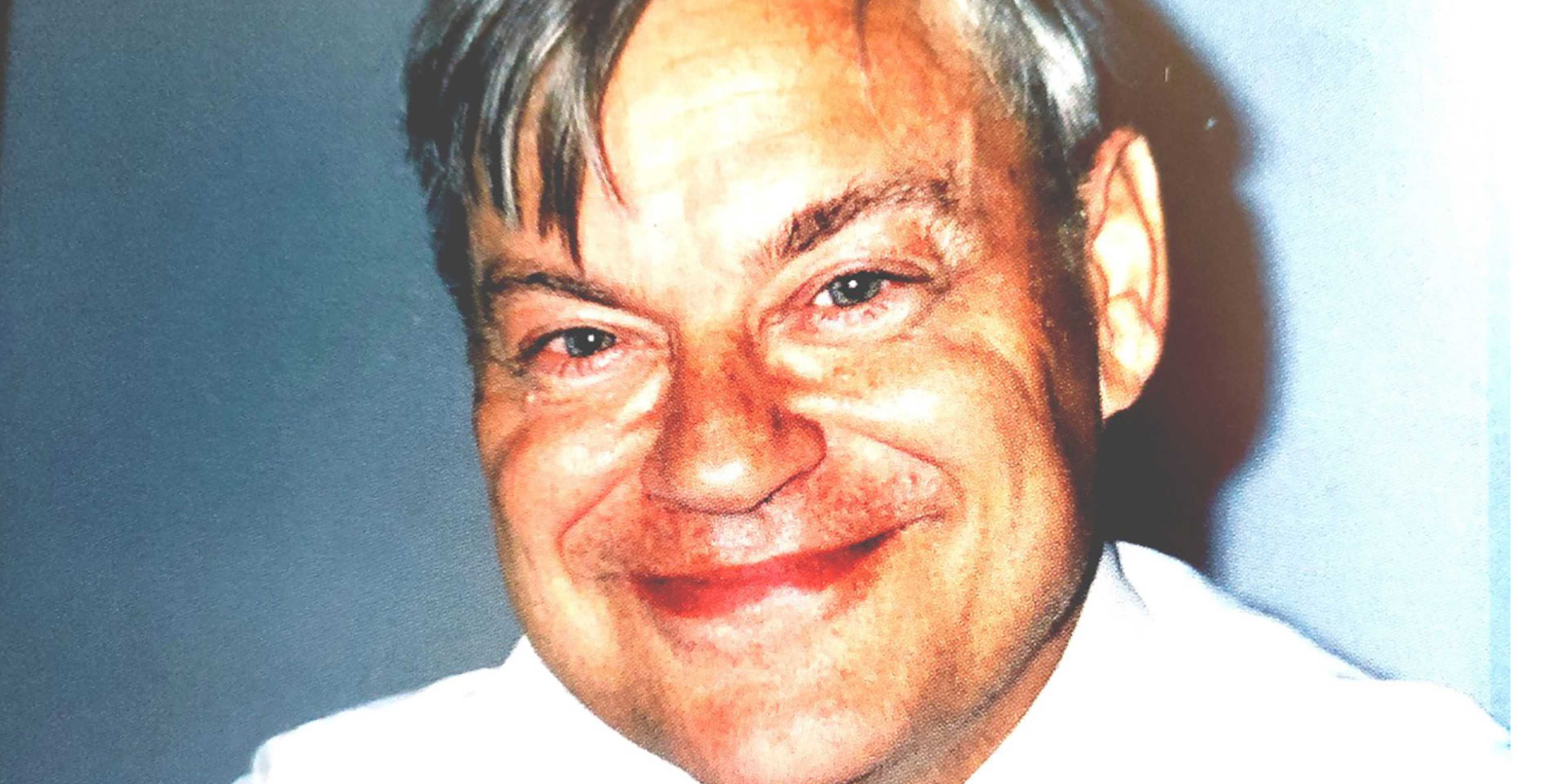 The image shows a close-up portrait of a smiling older man with gray hair and a friendly expression.