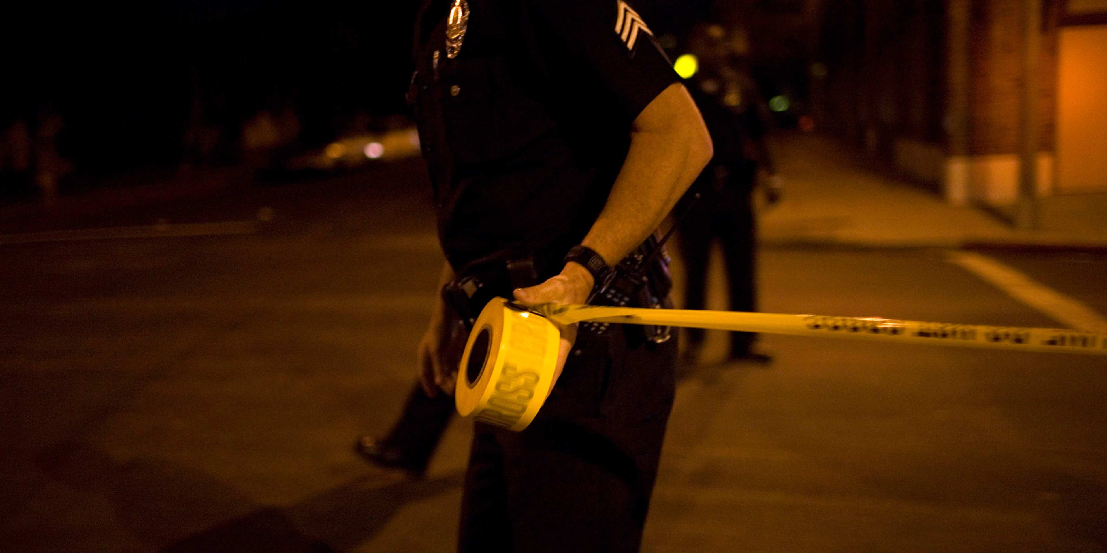 A dark, nighttime street scene with a yellow police tape barrier cordoning off an area, suggesting an incident or investigation taking place.