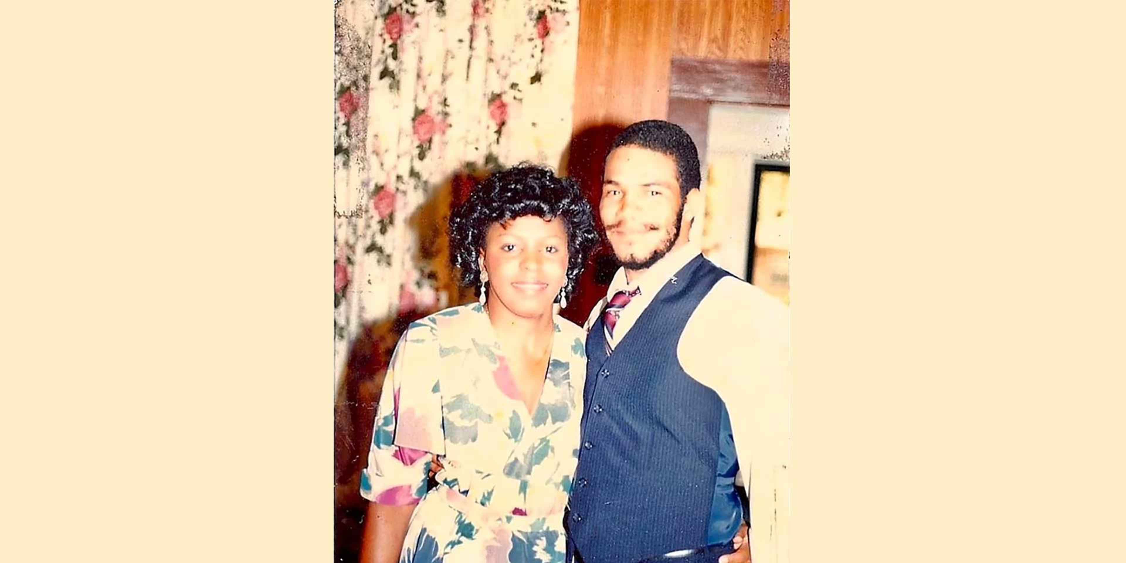 The image shows a couple posing together in what appears to be a formal setting, with a floral patterned background behind them.
