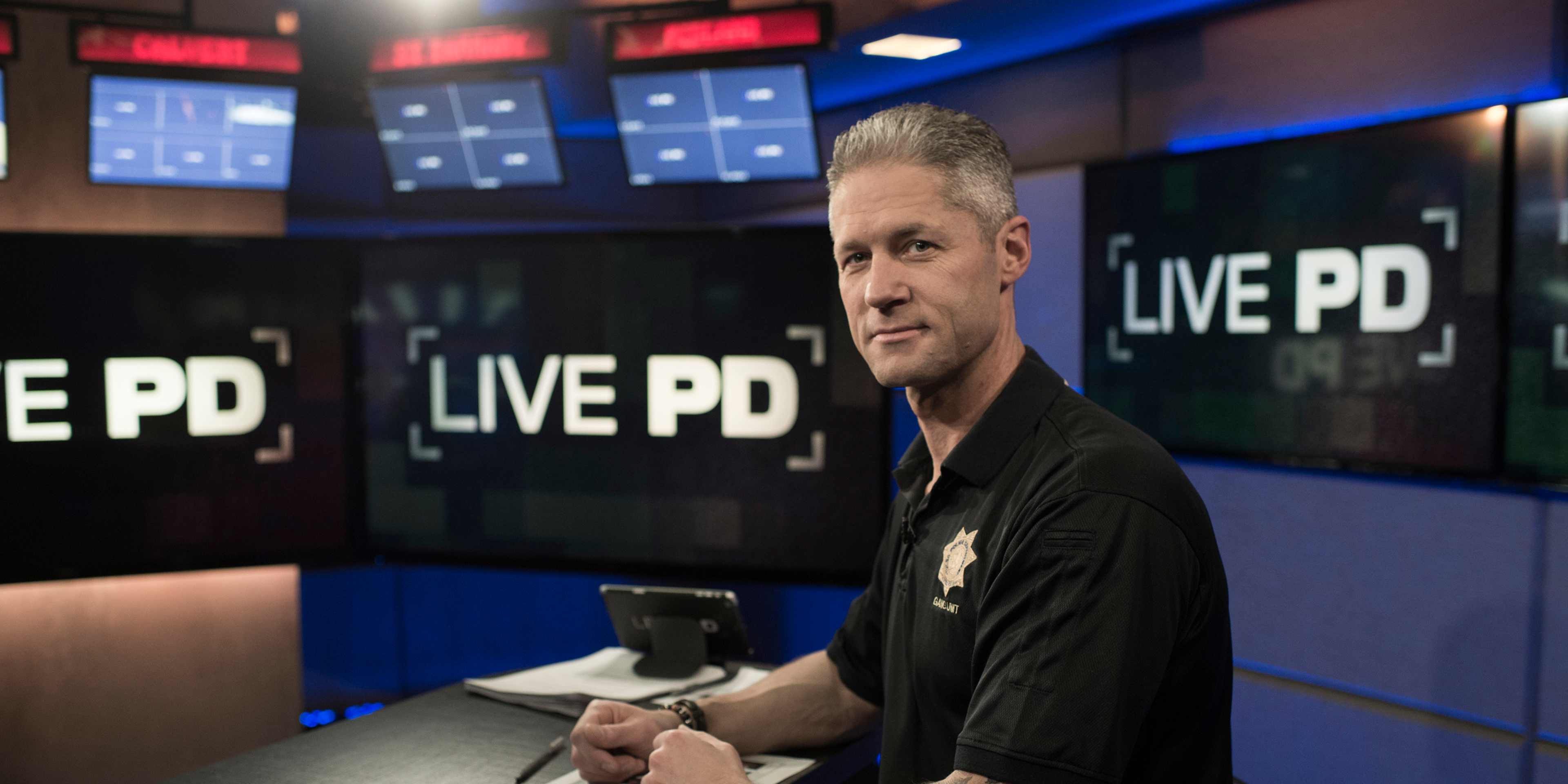 A man in a black uniform is sitting at a desk in a television studio, with "LIVE PD" displayed prominently in the background.