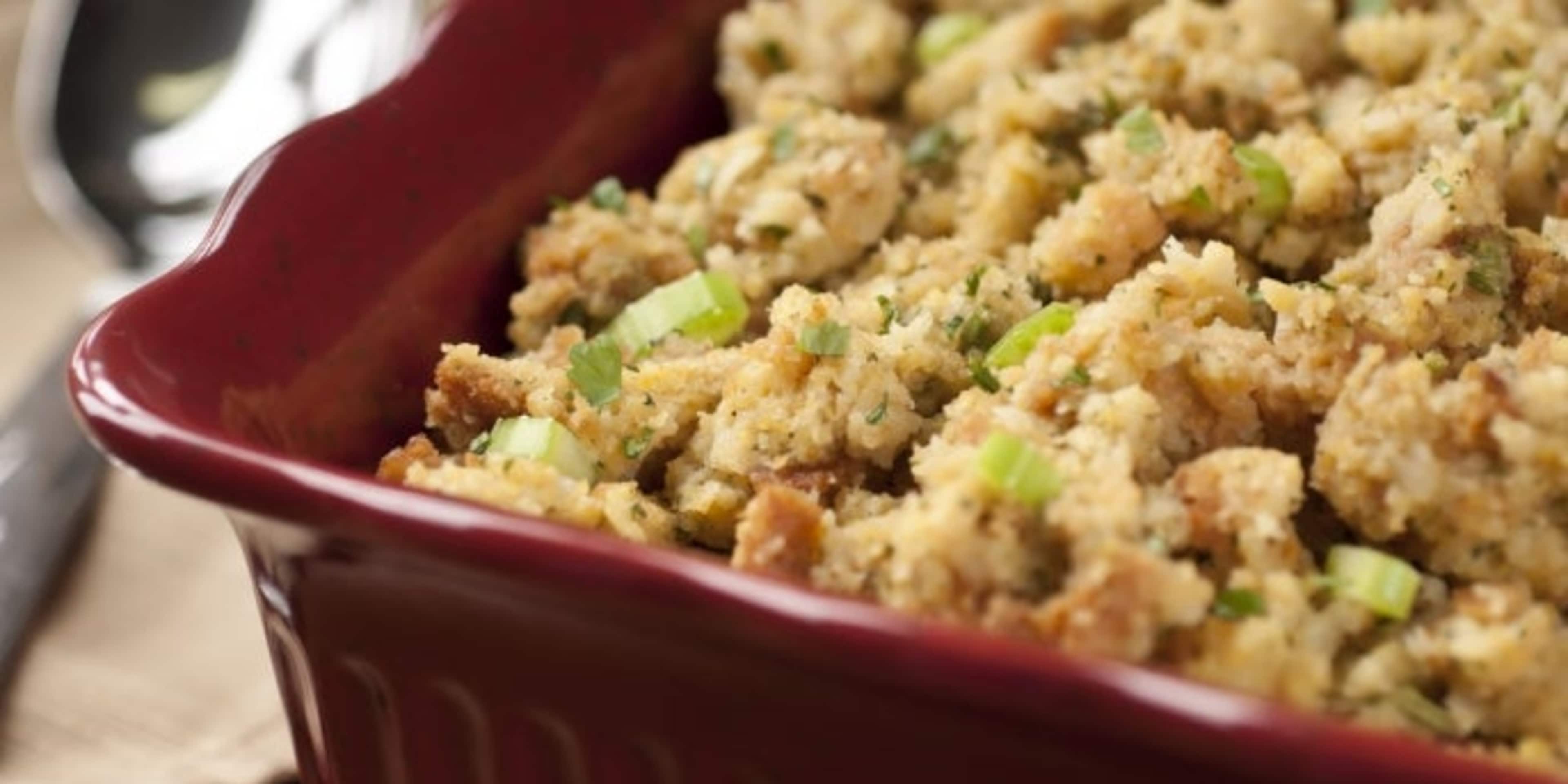 A red ceramic baking dish filled with a golden-brown crumbly mixture, likely a savory casserole or stuffing, sits on a wooden surface.