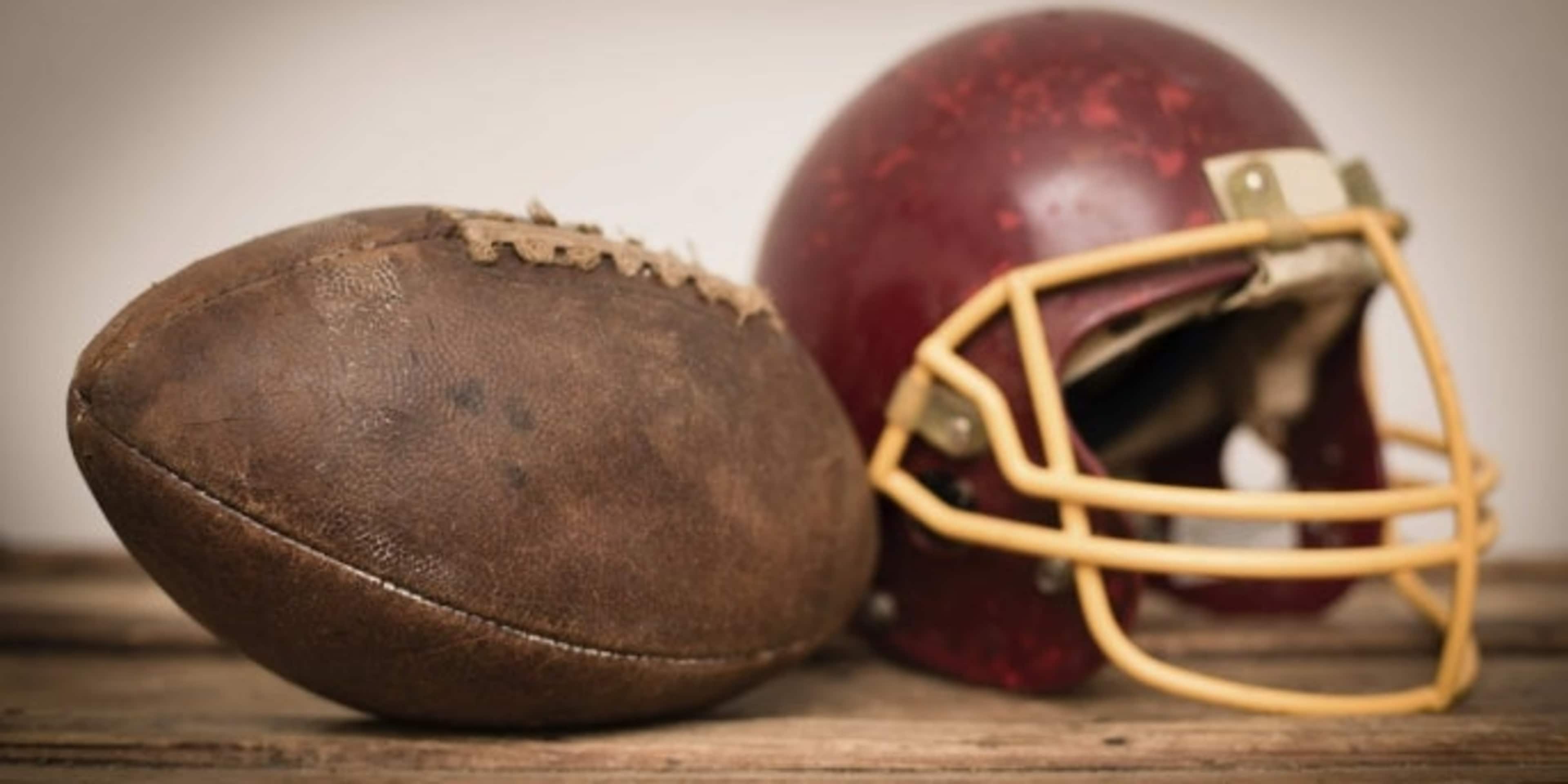 Close up, color image of a vintage football helmet and football, sitting on wood. Some desaturation and grain added for vintage feel.