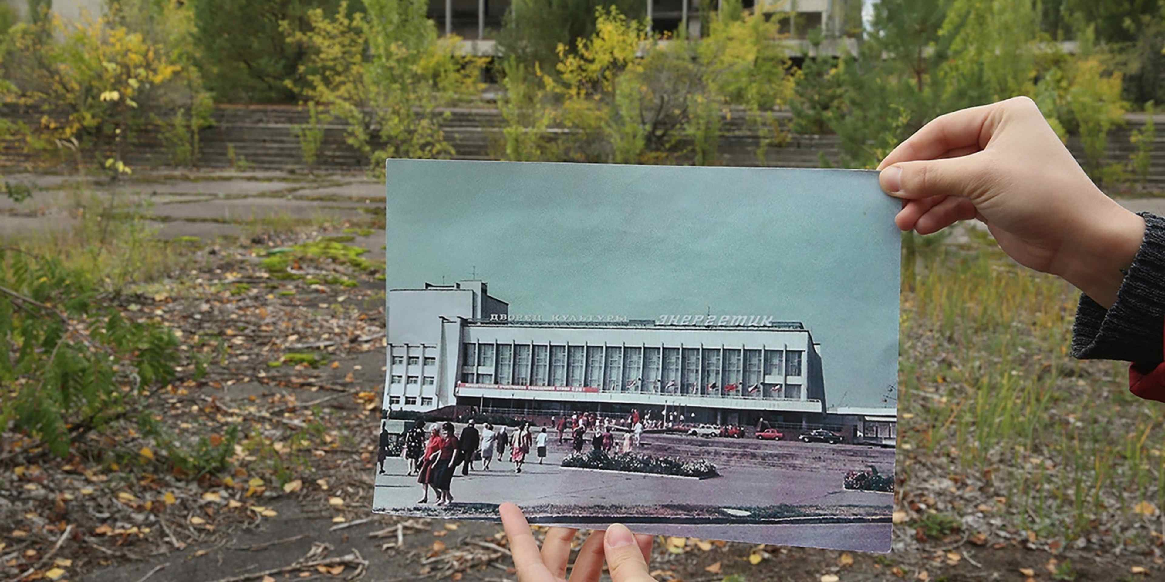 A person holds up a photo showing the city of Prypiat's main square and the 'Energetik' cultural center before the 1986 Chernobyl nuclear disaster, against the same site, now abandoned and overgrown with trees, 2015. (Credit: Sean Gallup/Getty Images)