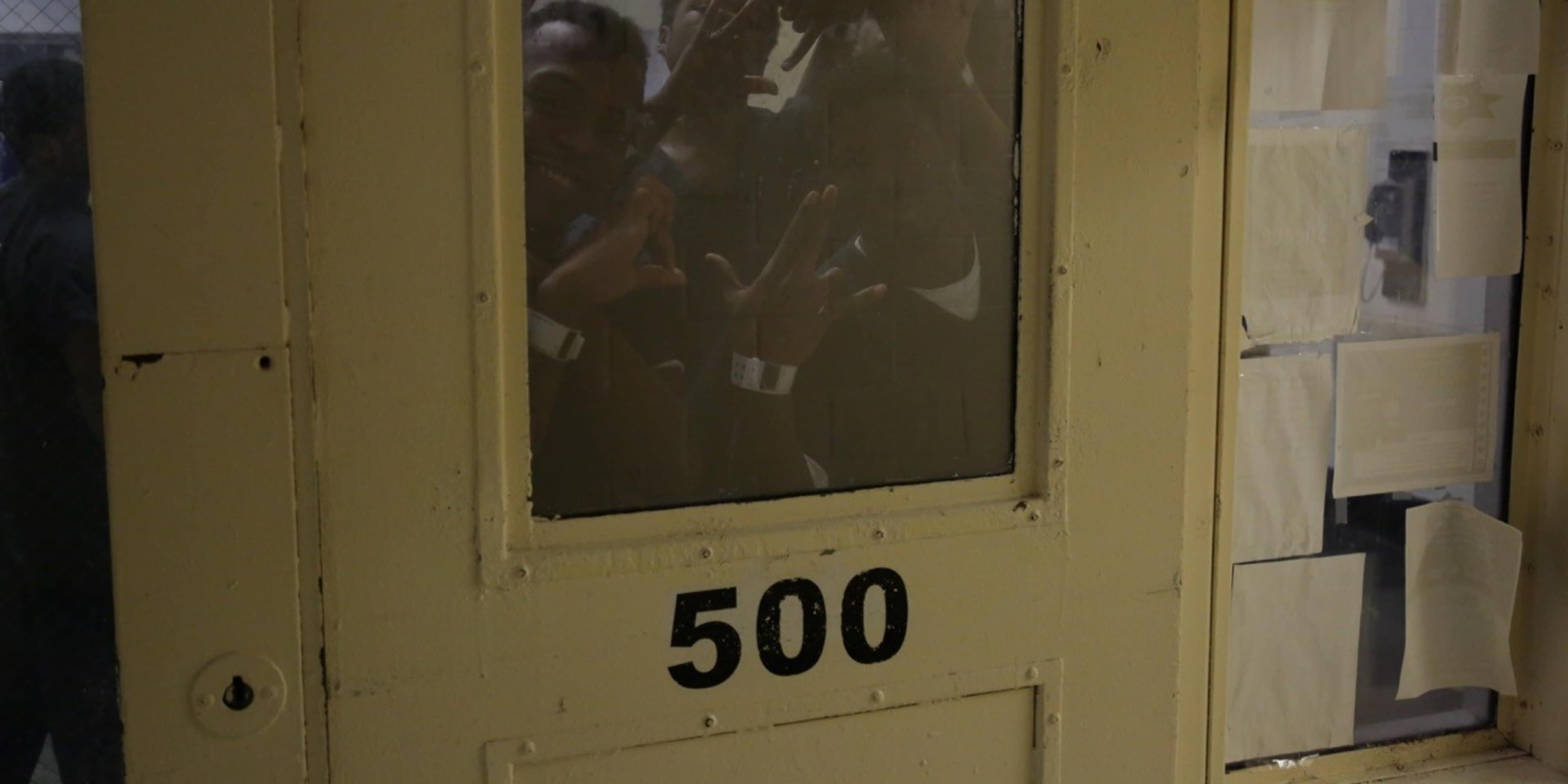 The image shows a wooden door with the number "500" painted on it, and a framed image or poster visible through the glass panel of the door, depicting what appears to be a group of people or figures.