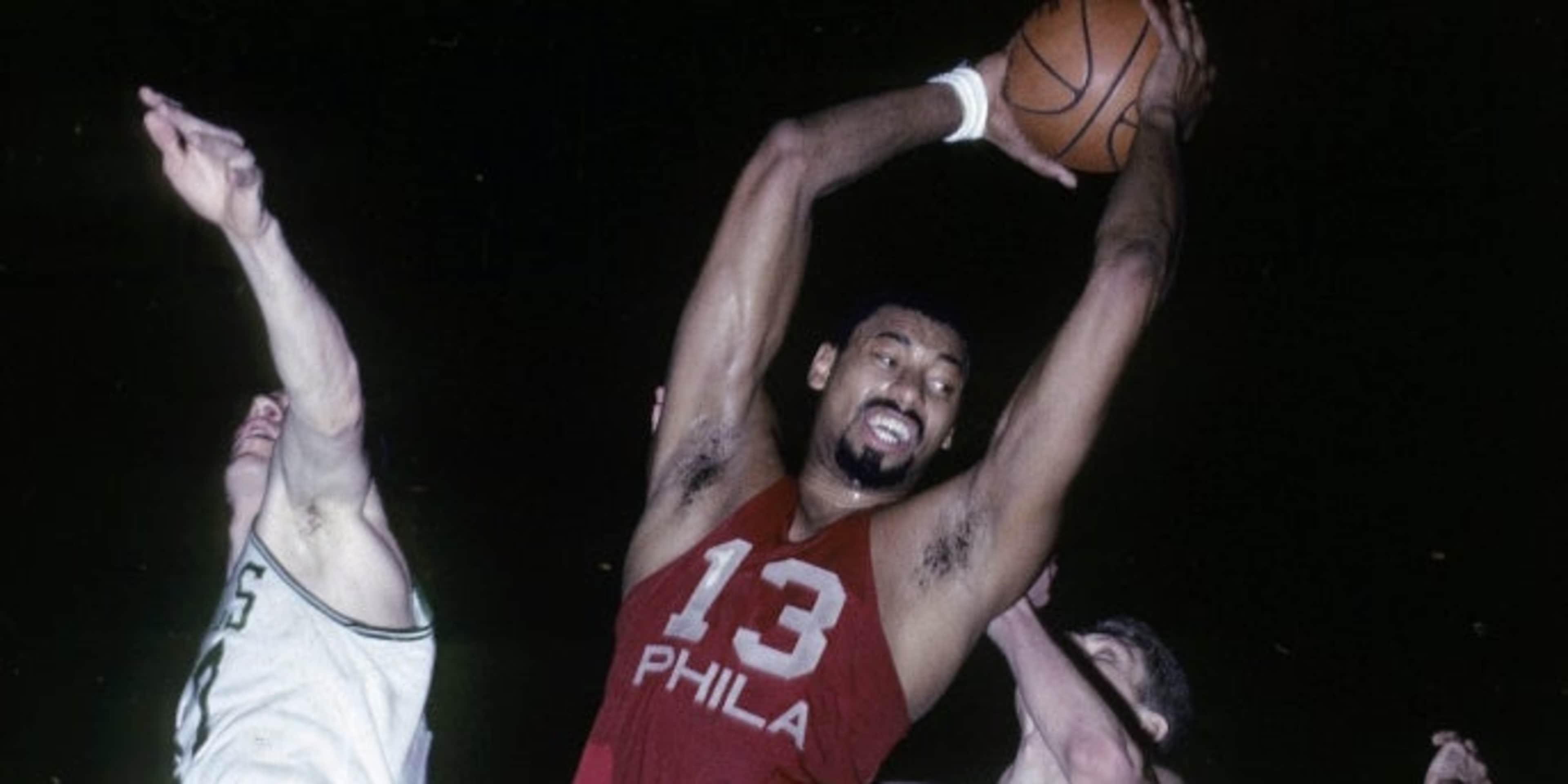 Wilt Chamberlain of the Philadelphia 76ers pulls down a rebound against the Boston Celtics during a mid-1960s game at Boston Garden. (Credit: Focus on Sport/Getty Images)