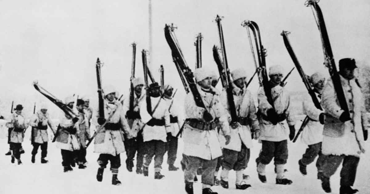 Finnish soldiers wearing full white winter camouflage uniforms marching through the snow