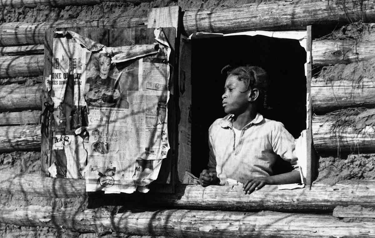 African American Girl Posing in Log Cabin Window(Original Caption) The late Arthur Rothstein was a perceptive photographer who captured life in rural America of the 1930's with a journalistic style that helped raise national awareness. His photograph, Gee's Bend Alabama, 1938, combines photographic excellence with a clear statement on black life of the era. This photograph is part of the exhibit, Blacks in America: A Photographic Record.