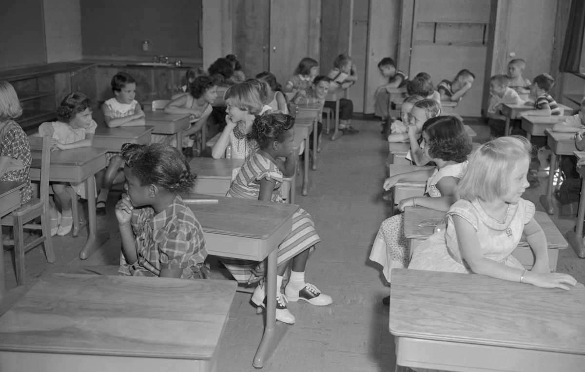 Kids in classroom on the first day of desegregation in Virginia, 1959. (Original Caption reads: 'A Negro child and a white child face each other on the first classroom day in history that saw racial integration in some public schools in the southern states of the U.S. This classroom is the third grade of the Fort Myer Elementary School, which is operated for children of military personnel. The end of segregation in this school and and in one at Fort Belvoir, Va., came with a Defense Department order to that effect'.