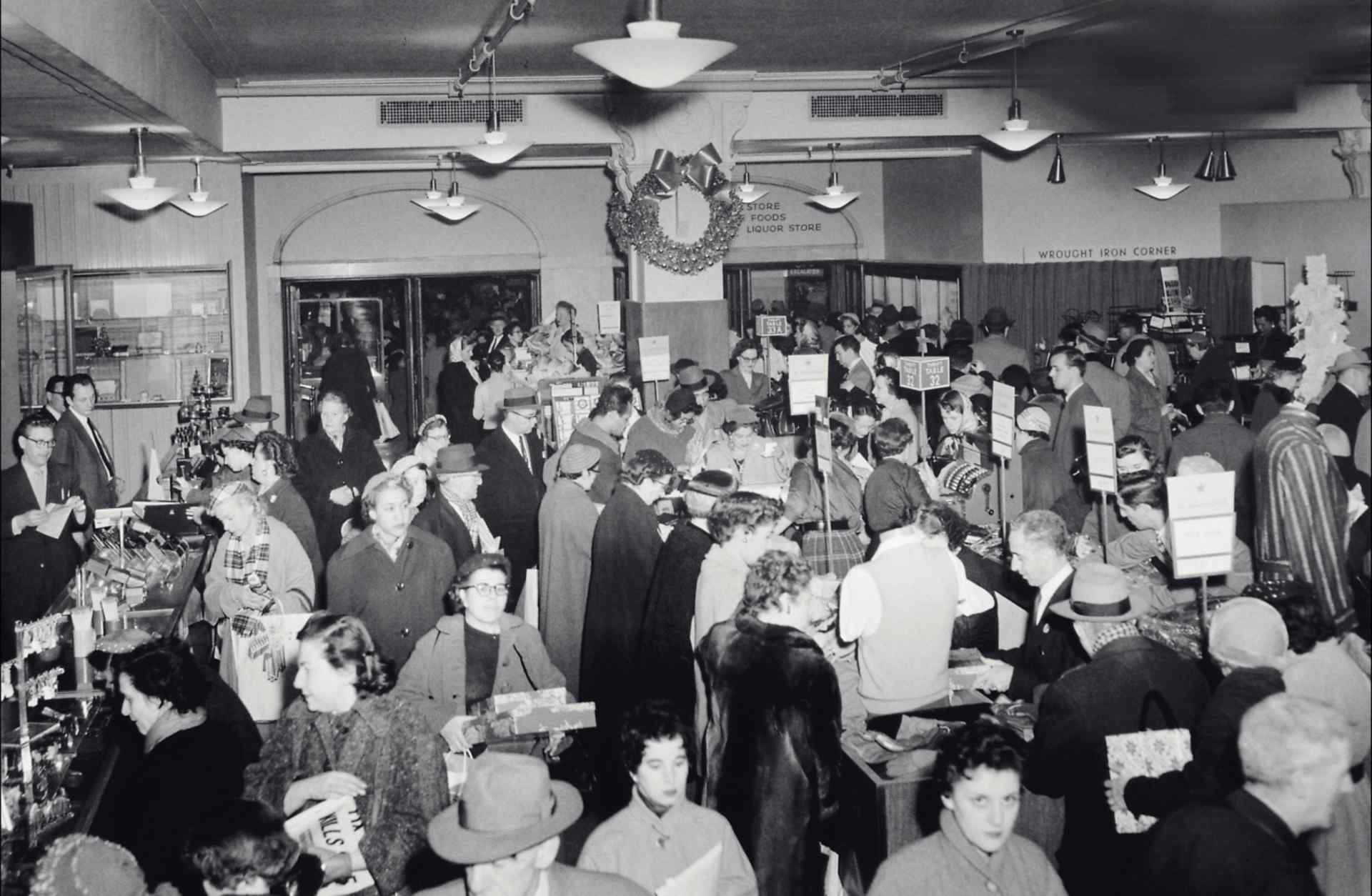 Bird's eye view of a crowd of people standing and roaming inside a department store that is decorated for Christmas