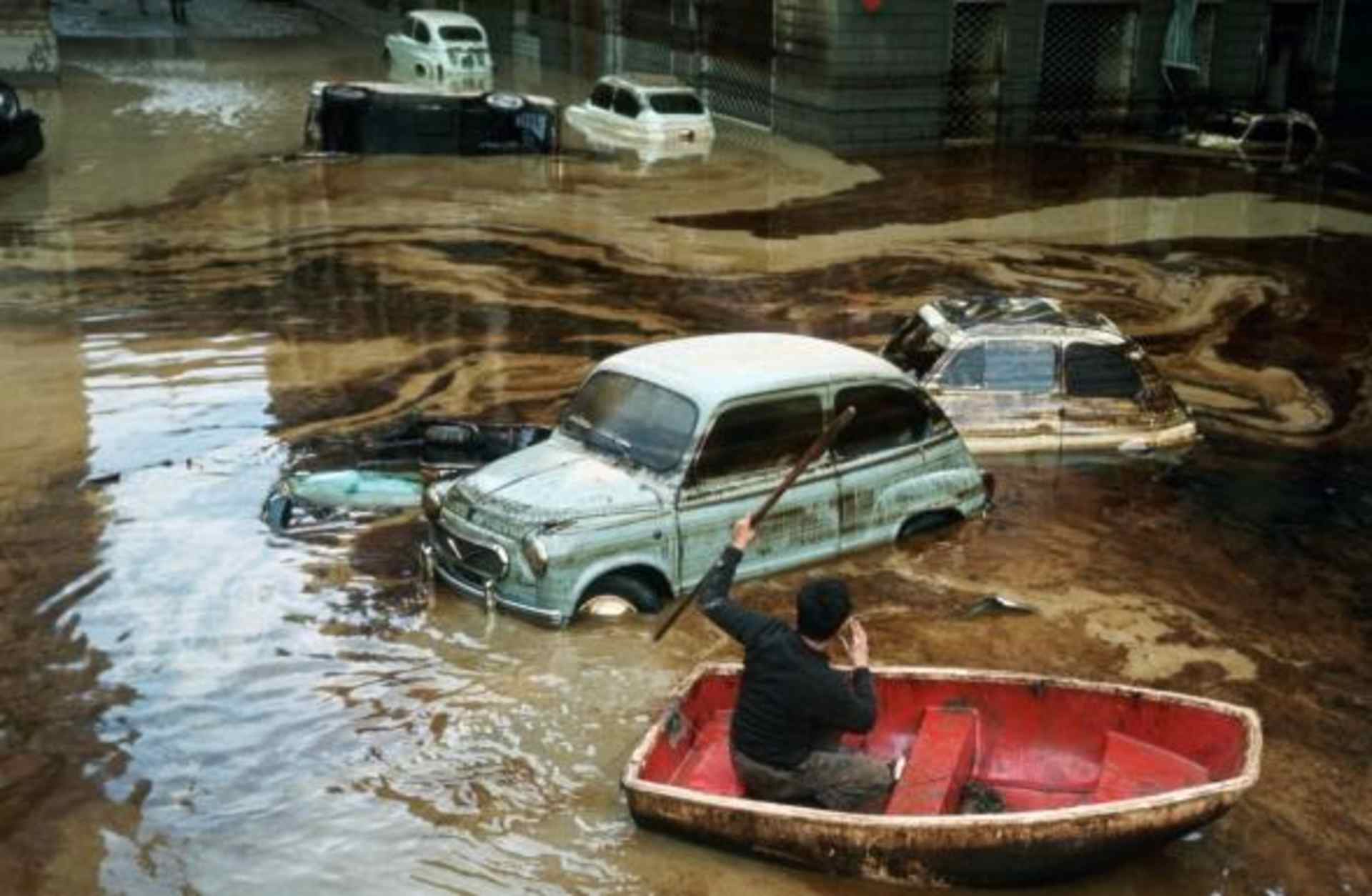 A man paddles a small boat among wrecked cars on a waterlogged street in Florence, following the devastating flood of November 1966, during which the water of the Arno rose as high as 20 feet, submerging sculpture, paintings, mosaics and manuscripts in the city's libraries. (Credit: Vittoriano Rastelli/Corbis via Getty Images)