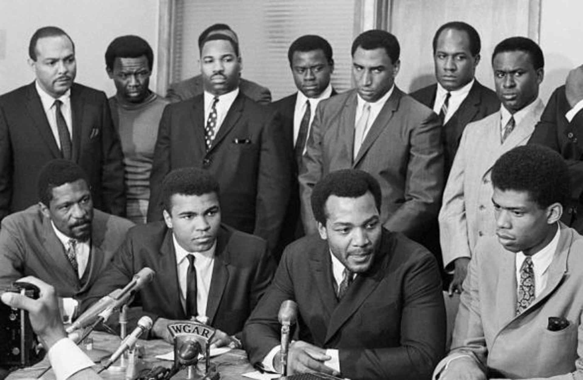 African American athletes and politicians at a press conference in support of Ali's decision. Front row: Bill Russell, Ali, Jim Brown and Kareem Abdul-Jabbar (then known as Lew Alcindor). Back row: Carl Stokes, Walter Beach, Bobby Mitchell, Sid Williams, Curtis McClinton, Willie Davis, Jim Shorter and John Wooten.