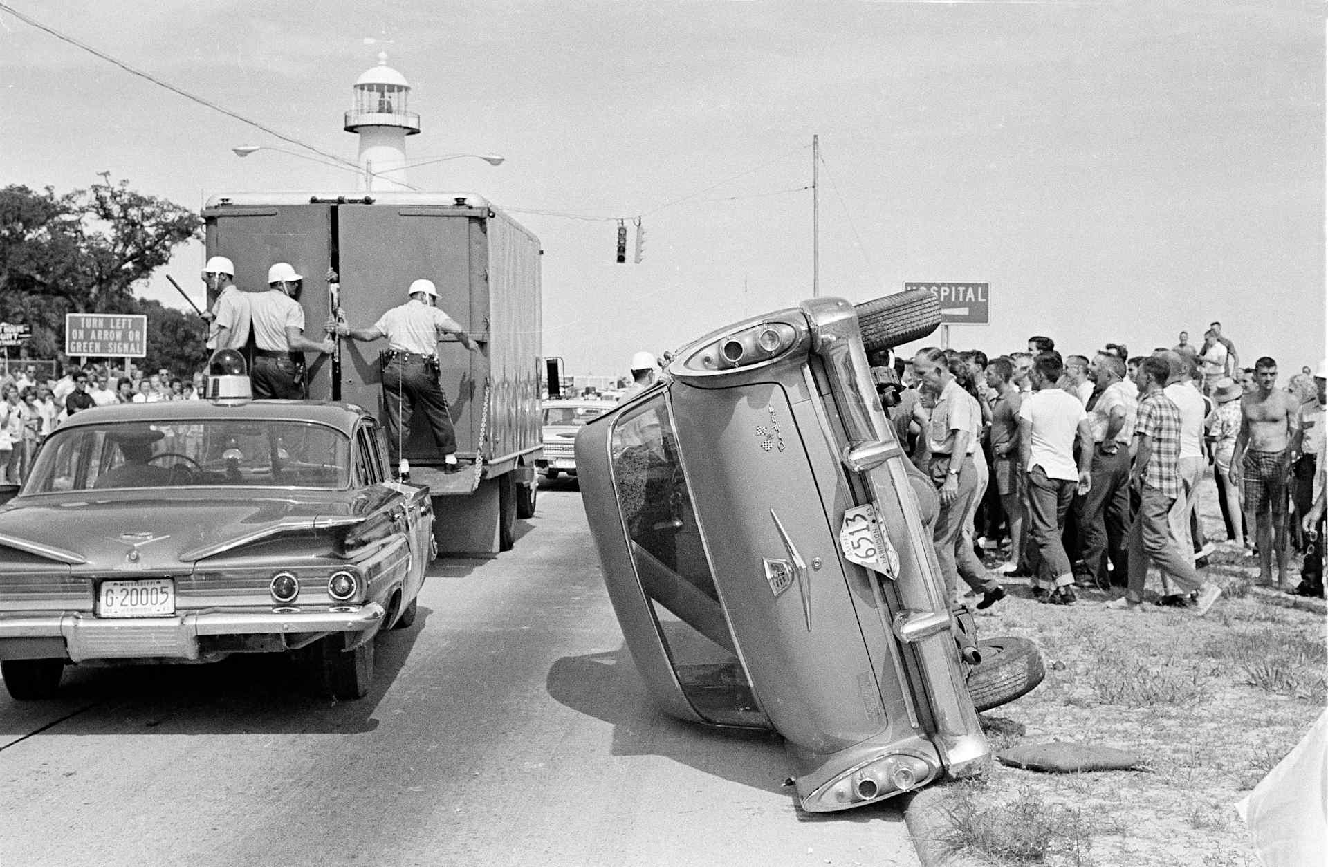 Jeering white men overturned this car belonging to Black demonstrators during their arrest in Biloxi, Miss., June 23, 1963, while attempting to desegregate the Gulf Coast beach. Sixty-five people of both races were arrested in the attempt.