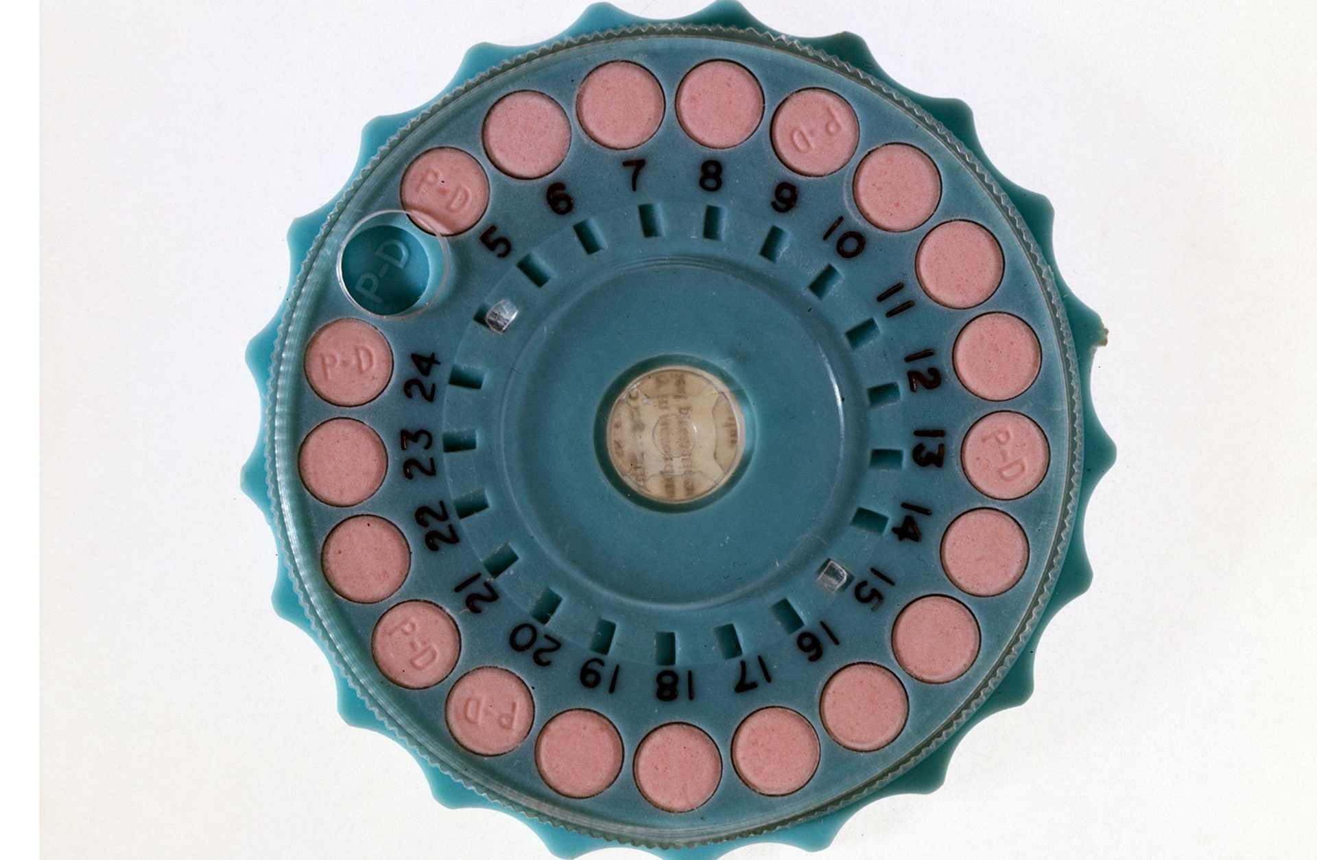 Pink contraceptive pills (marked 'PD') in a circular blue plastic dispenser.