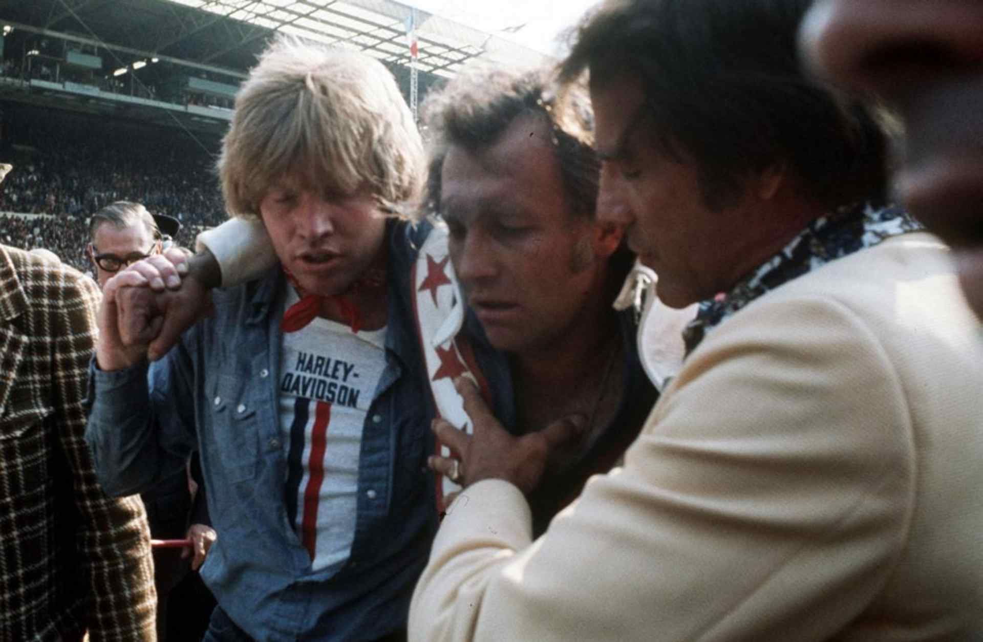 Evel Knievel being helped out of Wembley Stadium after he crashed during an attempt to jump 13 buses.