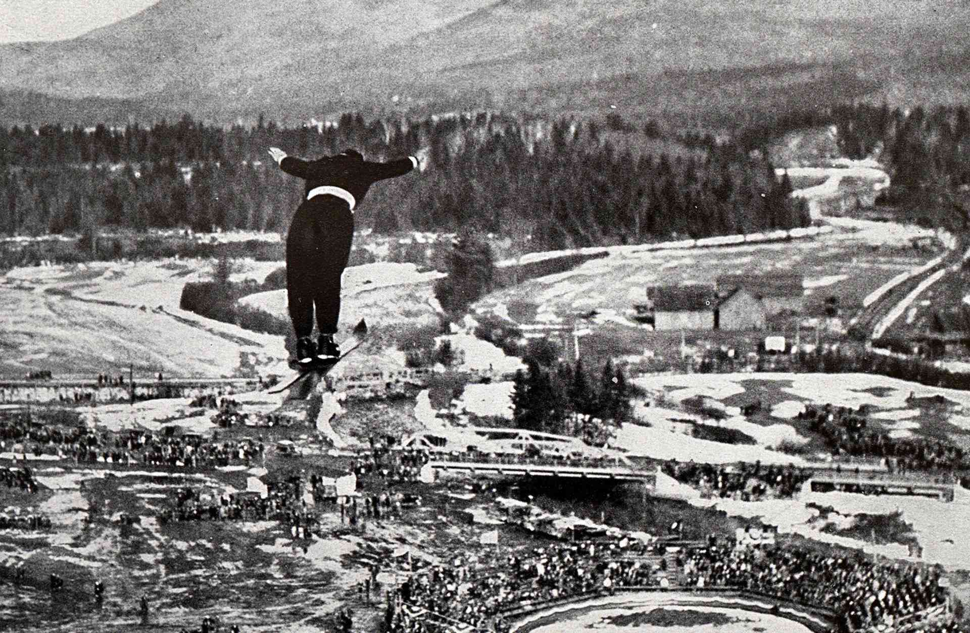 An athlete soars above barely snow-covered terrain in the ski jump competition at the 1932 Lake Placid Winter Olympics.