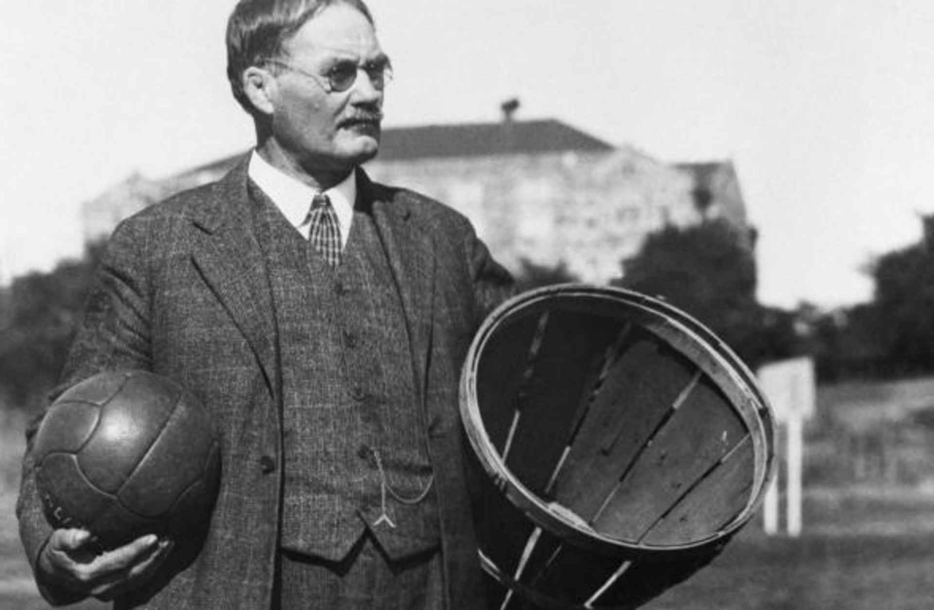 The inventor of basketball, Dr. James Naismith, stands in a field carrying a ball and a basket. (Credit: Bettmann/Getty Images)