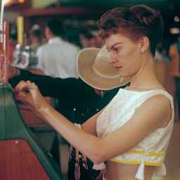 Las Vegas 1959. Young woman at a slot machine. A machine where you put in a coin and pull a lever that...
