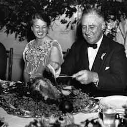 First Lady Eleanor Roosevelt and President Franklin D. Roosevelt smile while sitting at a table as Franklin slices a turkey