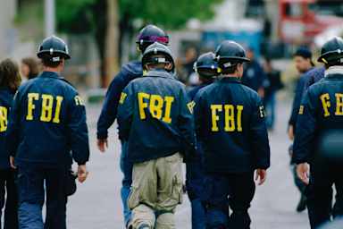 Five agents wearing hard helmets and FBI windbreakers, seen from the back.