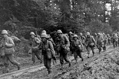 Japanese-American infantrymen of the 442nd Combat Team hike up a muddy French road to their new bivouac area, October 14, 1944.