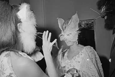 Vogue Editor Francoise Langlade (left) and Oscar de la Renta (right) in cat masks speaking with Anne McDonnell, wife of Henry Ford, in a butterfly mask.