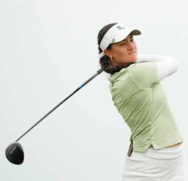 young dark-haired woman in golf attire and white visor swinging a big-headed golf club