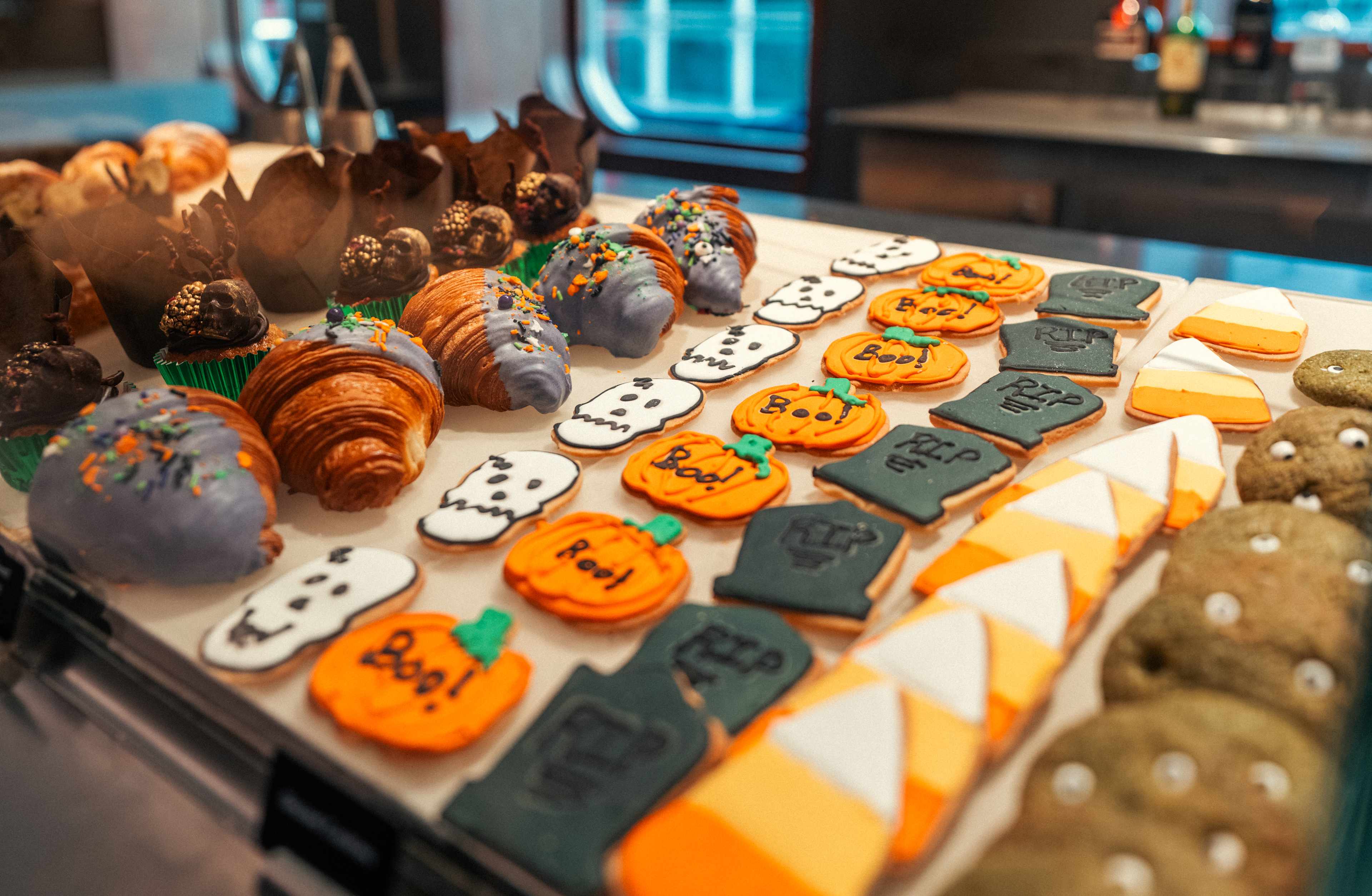 A display case filled with an assortment of colorful pastries, including macarons, cookies, and other baked goods, set against a backdrop of a dimly lit interior with visible shelving and seating areas.