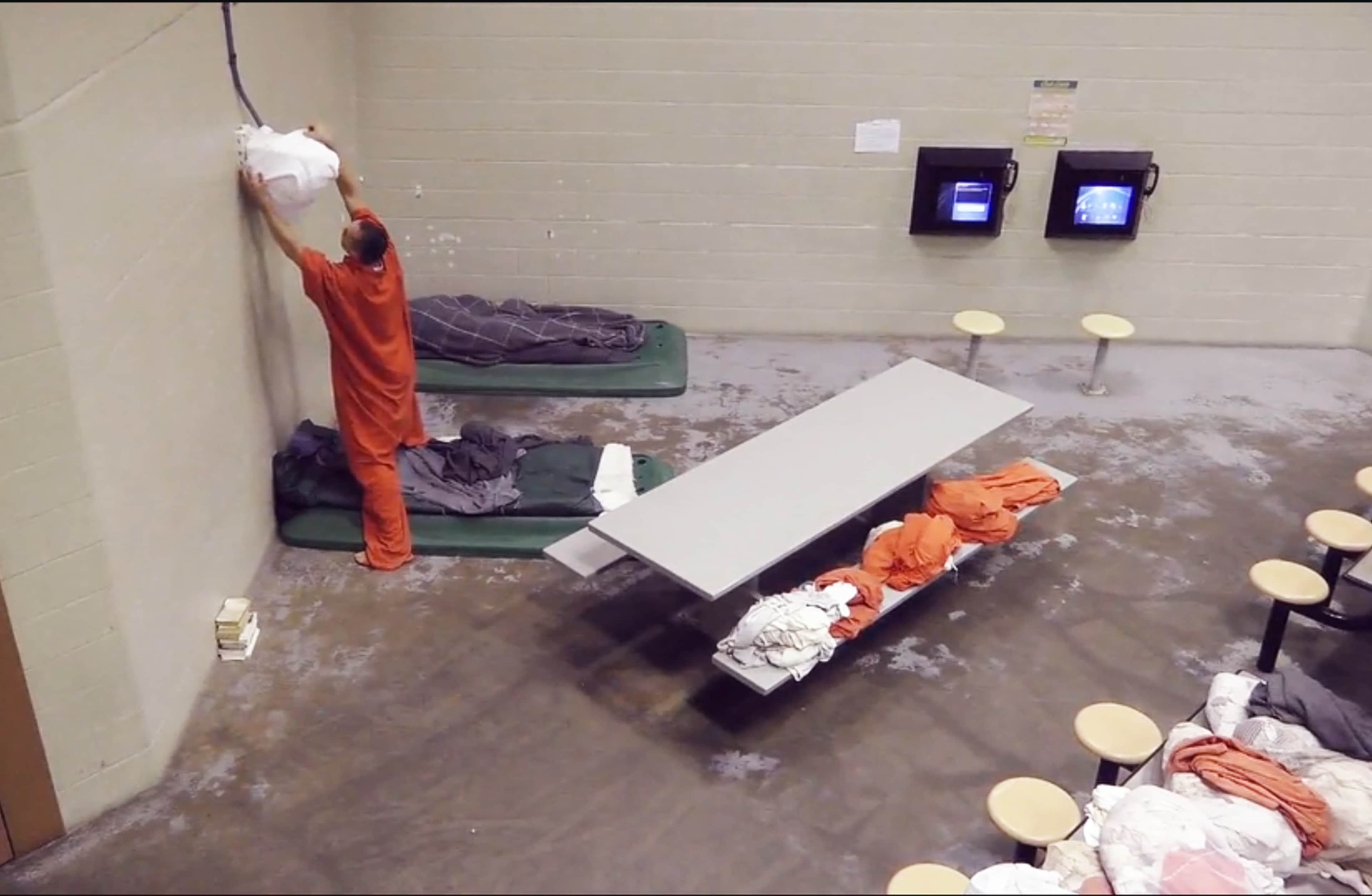 The image shows a cluttered room with various items scattered on the floor, including what appears to be a mattress, clothing, and other personal belongings.