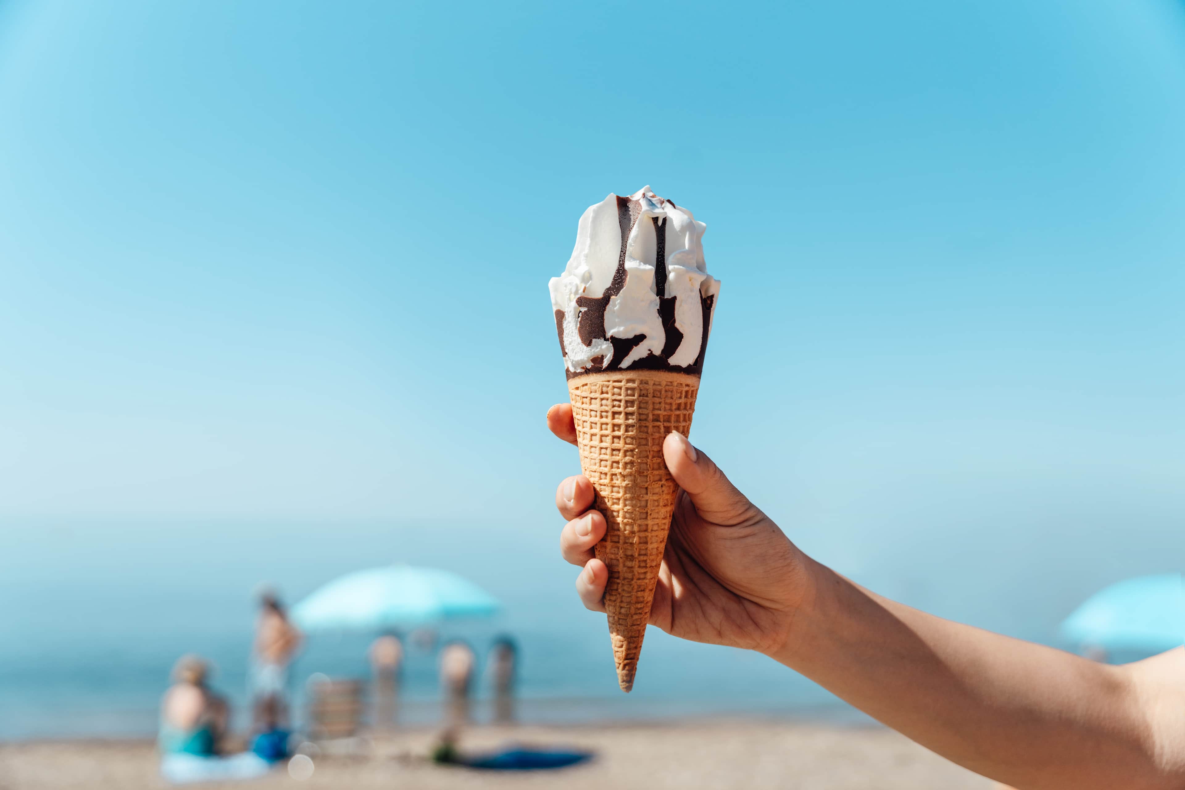Female hand holding ice-cream on the beach against clear blue sky