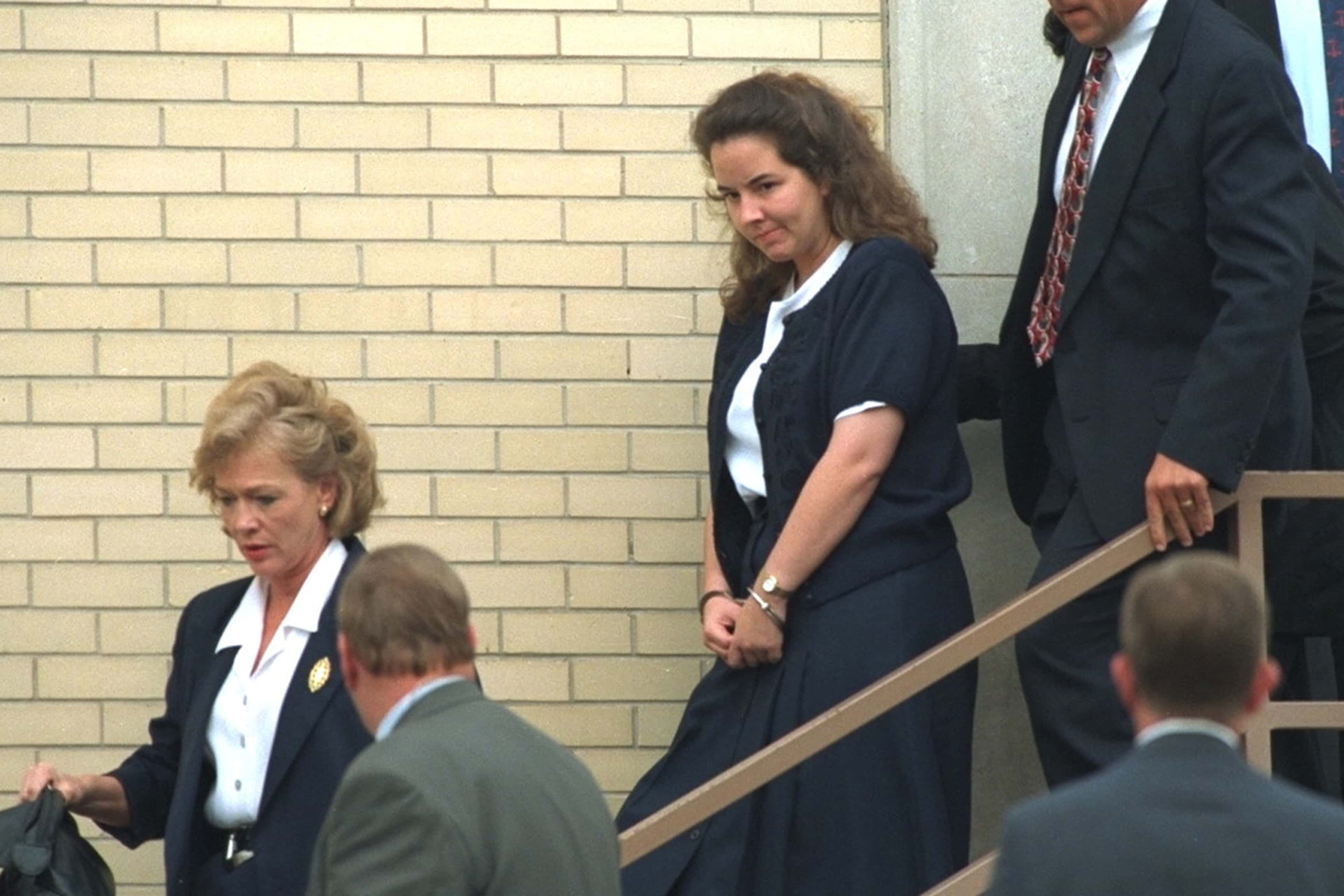 The image shows several individuals, some in formal attire, walking down a set of stairs in front of a brick building.
