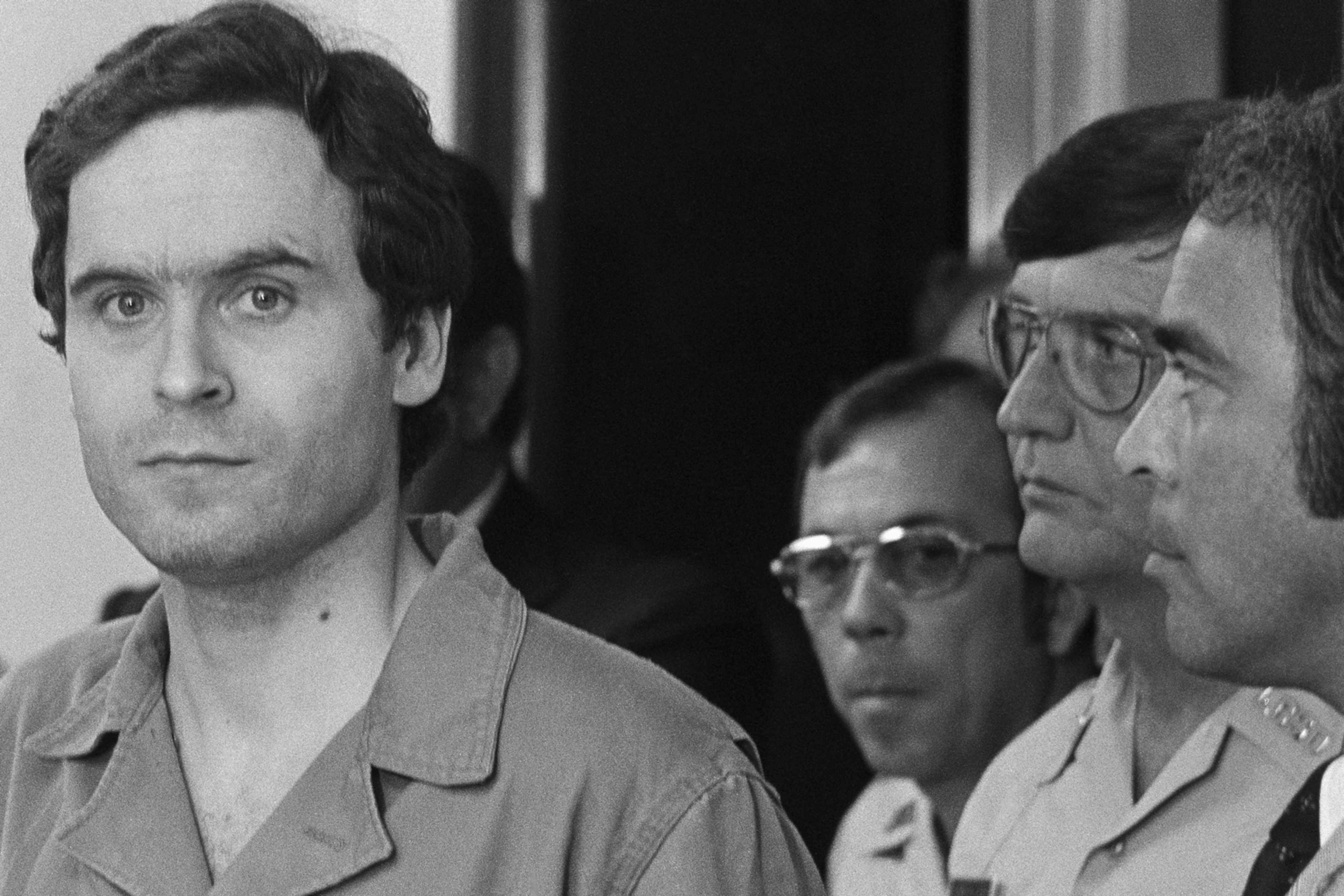 The image depicts a group of men, with one man in the foreground appearing to be the central figure, surrounded by several other men in the background.