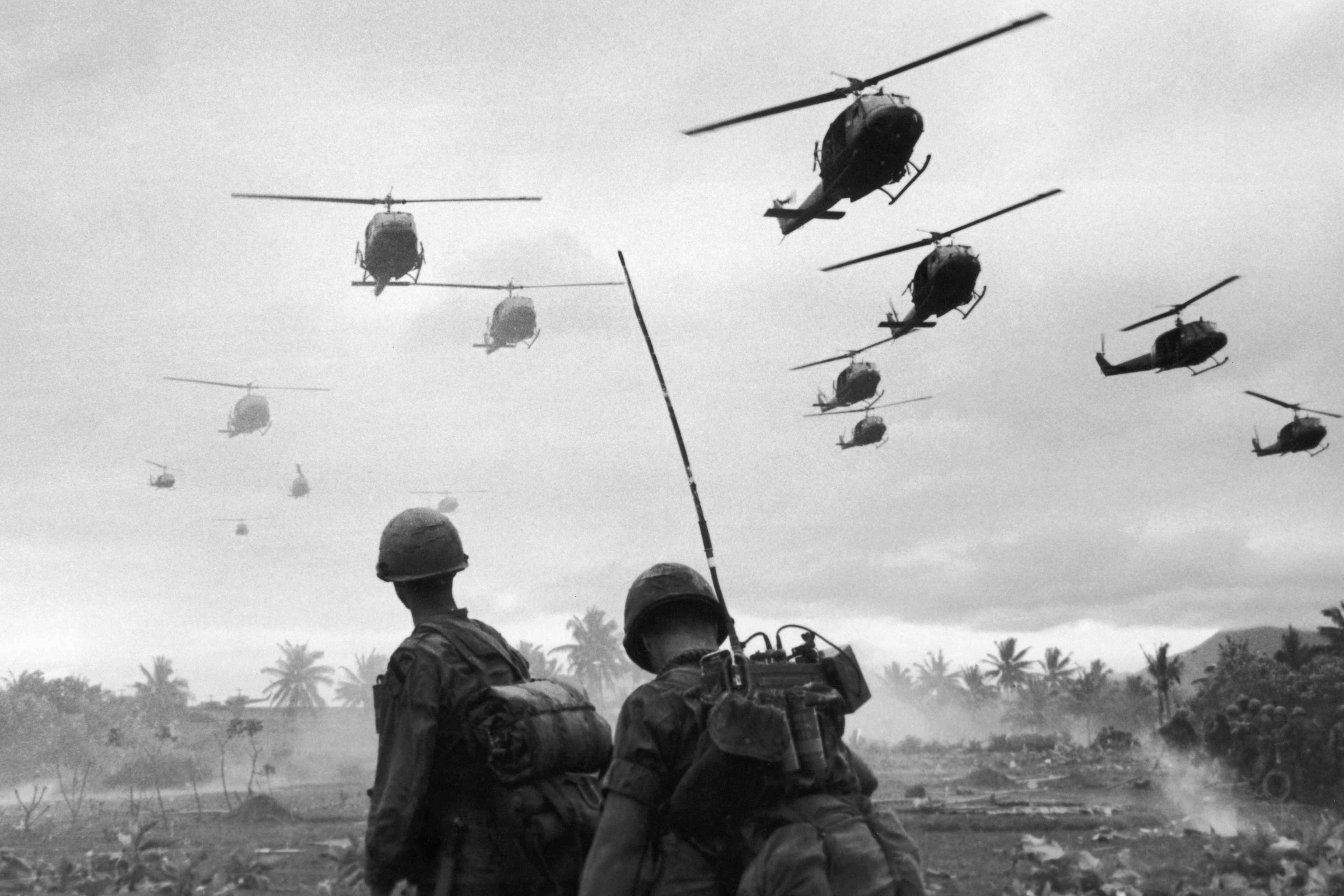 The second wave of combat helicopters of the 1st Air Cavalry Division fly over an RTO and his commander on an isolated landing zone during Operation Pershing, a search and destroy mission on the Bong Son Plain and An Lao Valley of South Vietnam, during the Vietnam War. The two American soldiers are waiting for the second wave to come in.