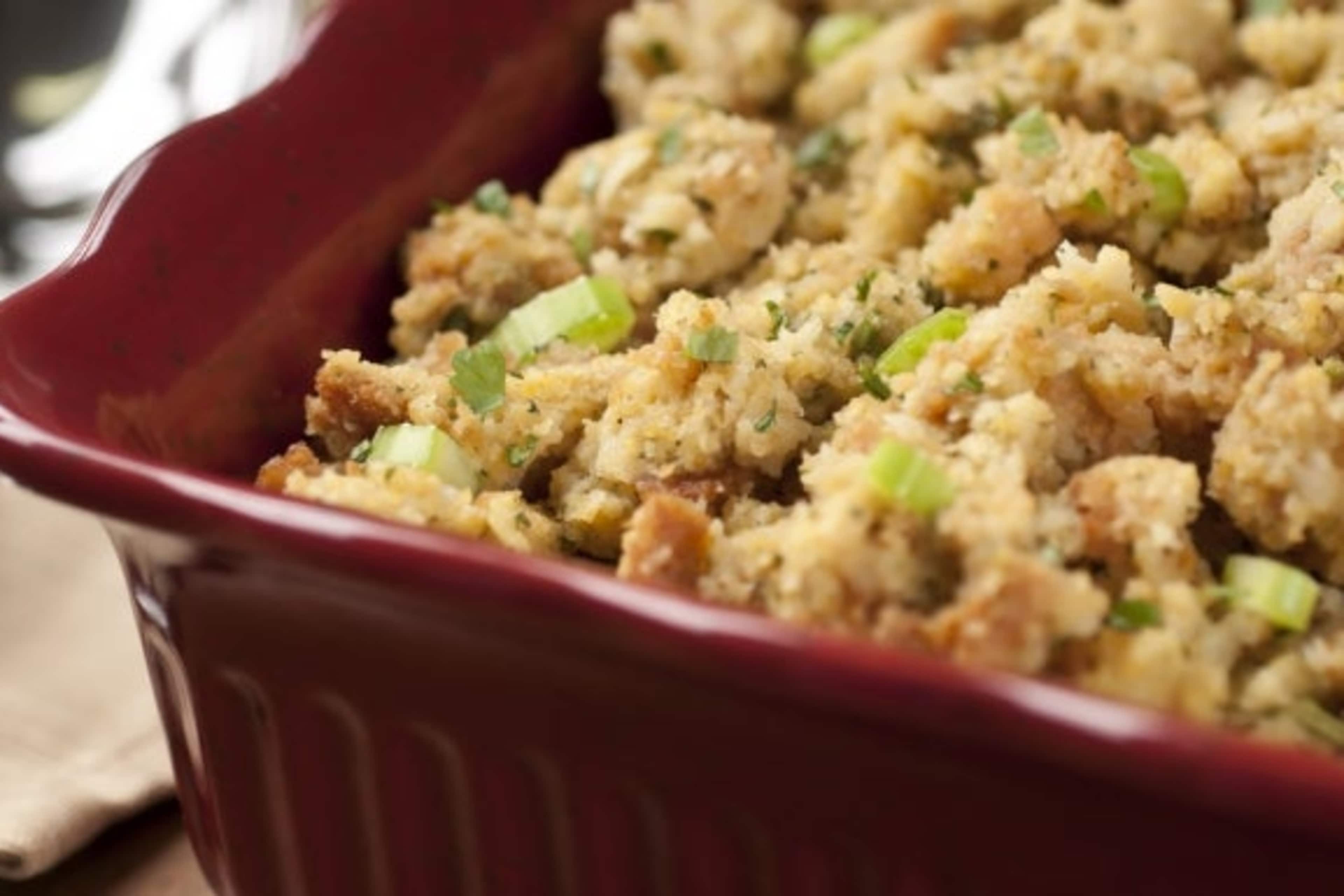 A red ceramic baking dish filled with a golden-brown crumbly mixture, likely a savory casserole or stuffing, sits on a wooden surface.