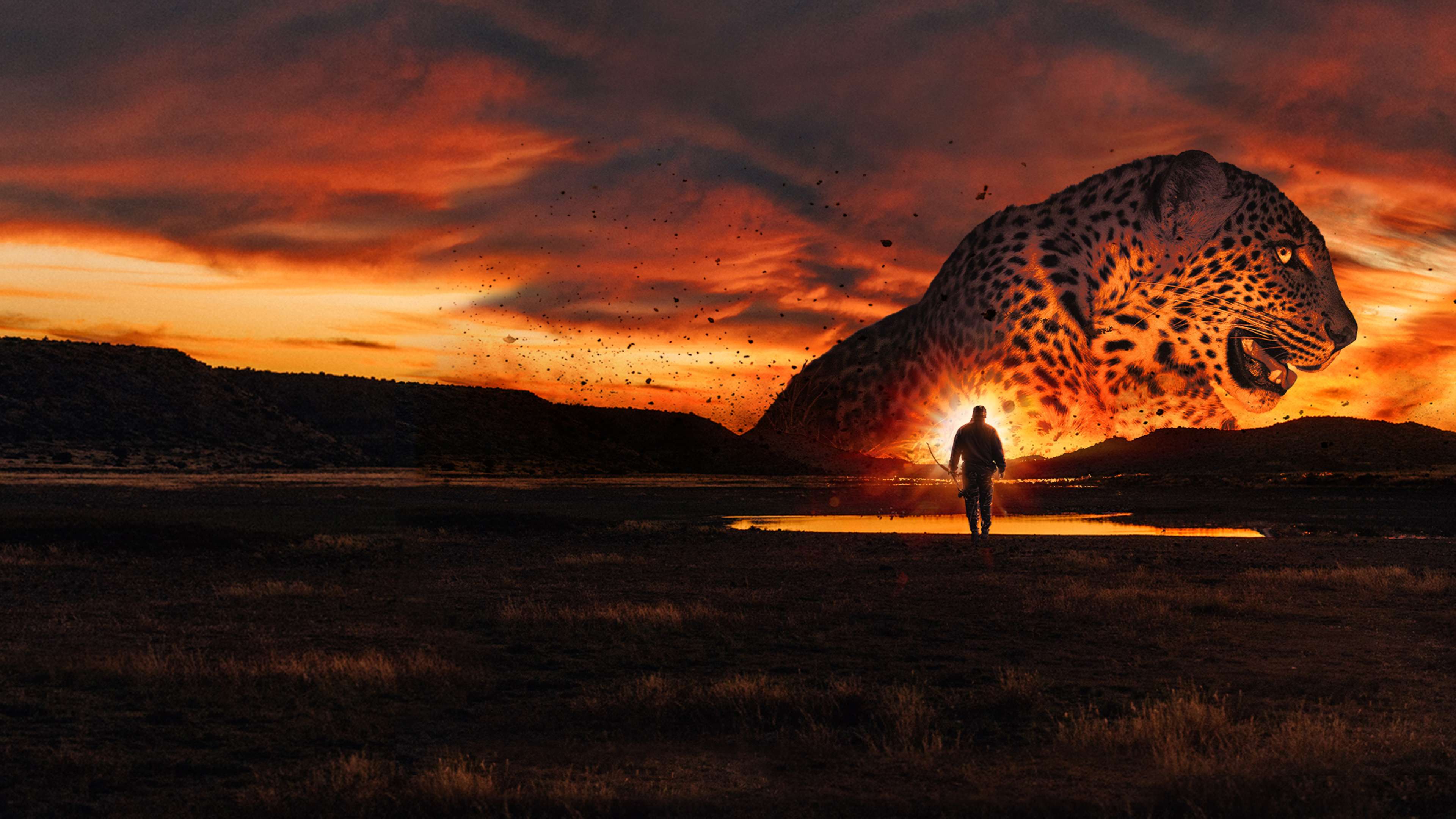 A lone figure stands in the foreground against a dramatic, fiery sunset sky, with a massive, leopard-patterned rock formation looming in the background.