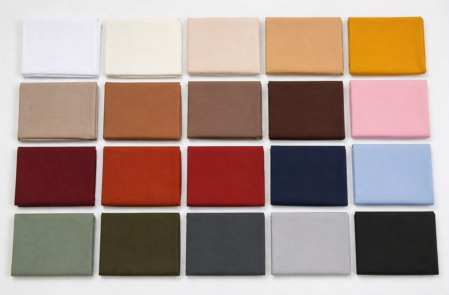 Overhead flat lay of solid dyed poplin fabric swatches in multiple uniform colors on white surface