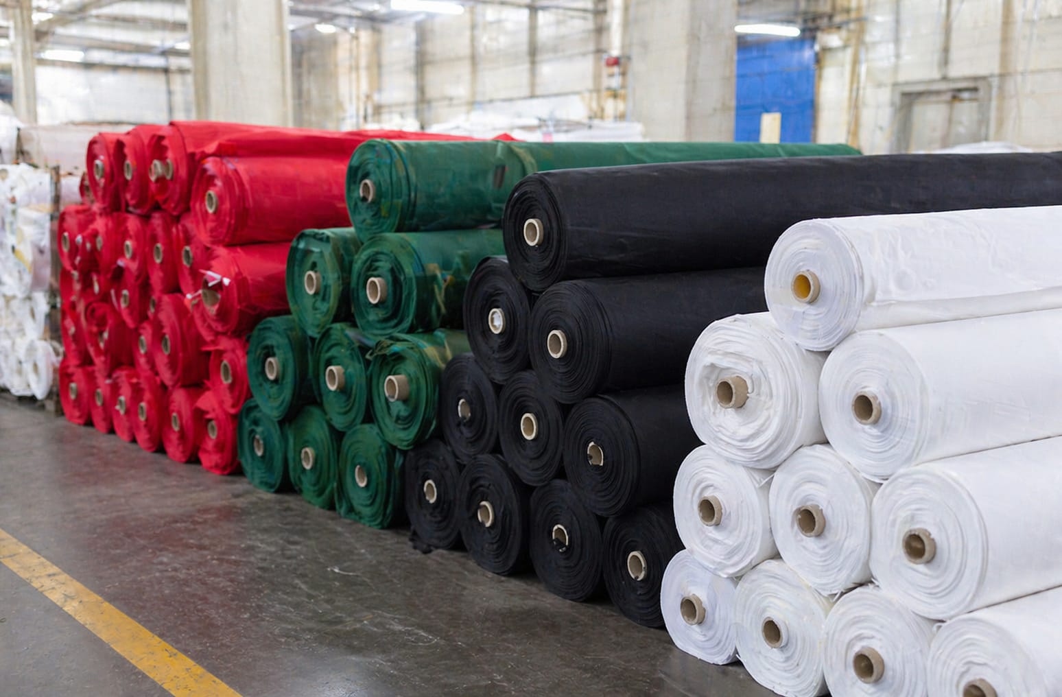 Stack of freshly manufactured solid dyed poplin fabric bolts in bold uniform colors on factory floor