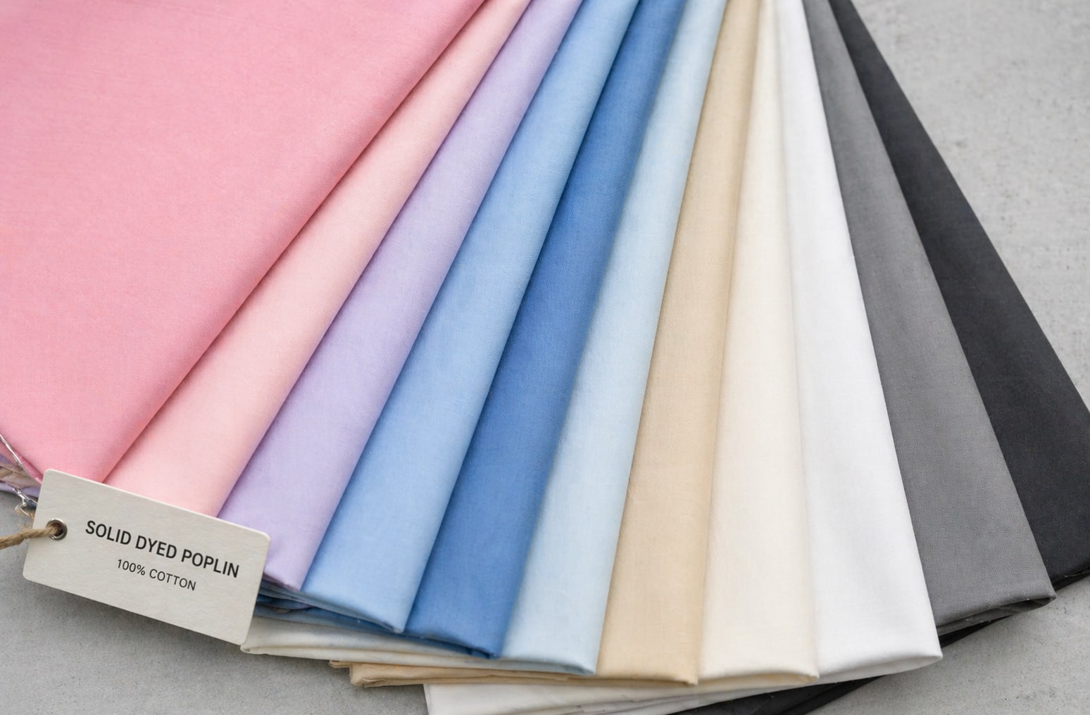 Flat lay of solid dyed poplin fabric samples in pastel and neutral color spectrum on grey surface