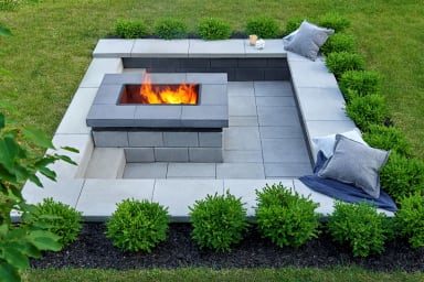 Stone outdoor fireplace with seating on a landscaped backyard patio Stone outdoor fireplace with seating on a landscaped backyard patio