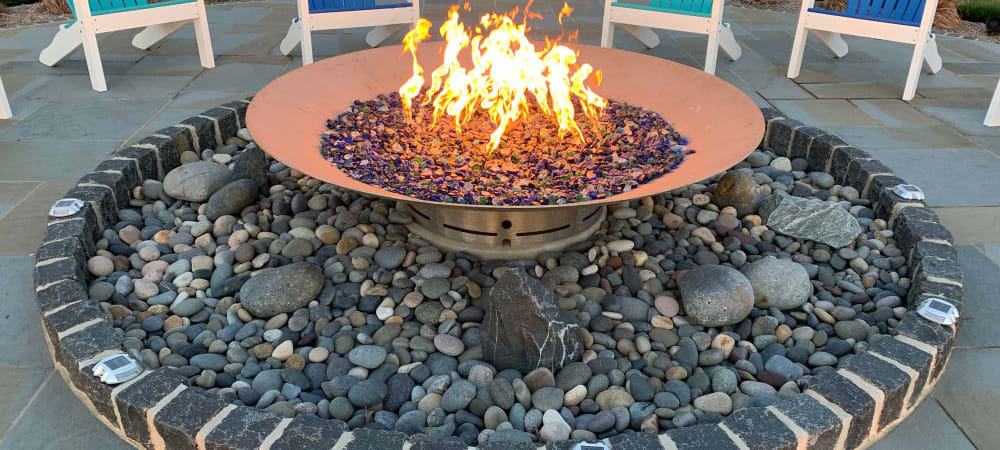 Custom Fire Pit with blue recycled glass, is surrounded by beach pebbles, belgian block and bluestone.