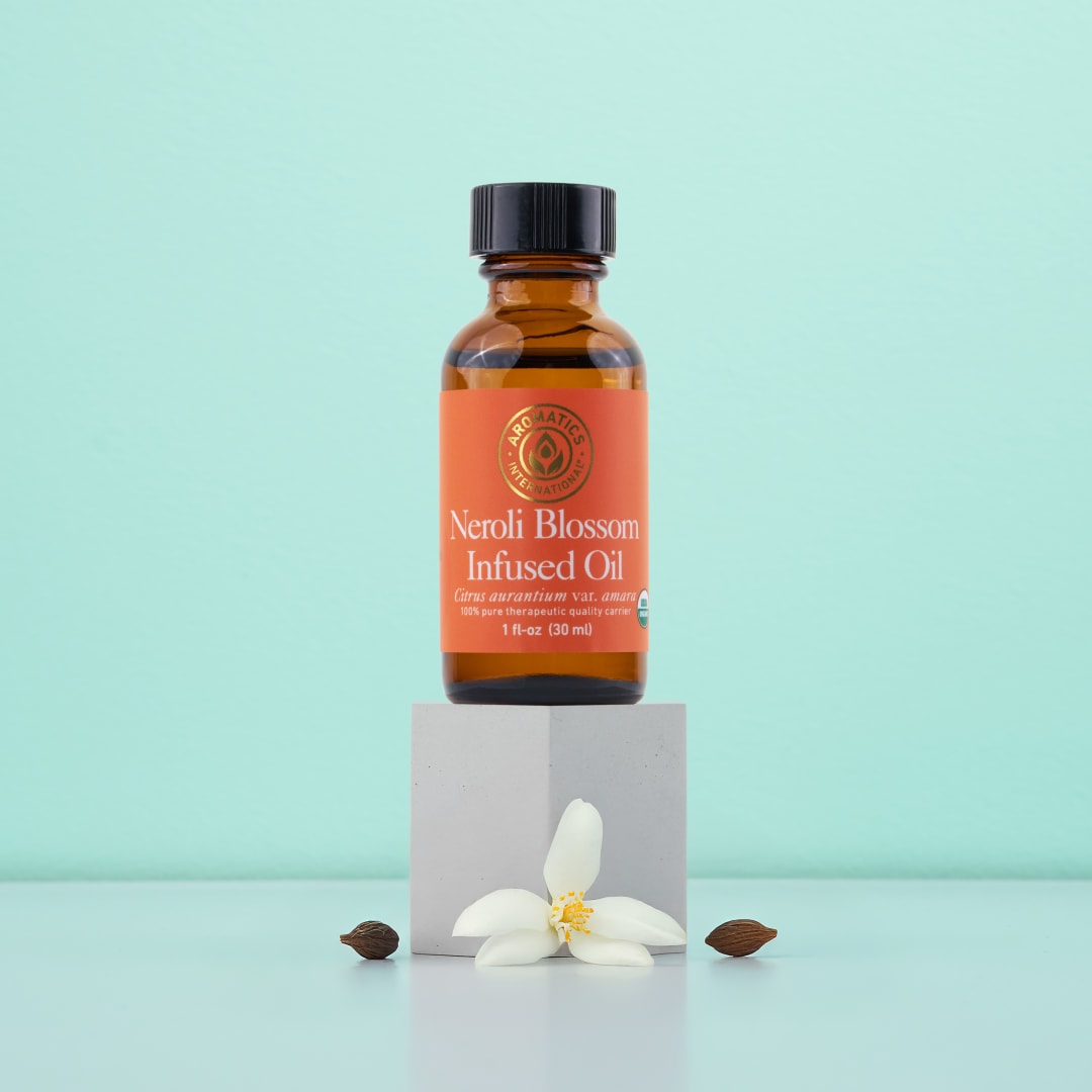 A bottle of Neroli Blossom Infused Jojoba Oil with a fresh neroli blossom and jojoba seeds