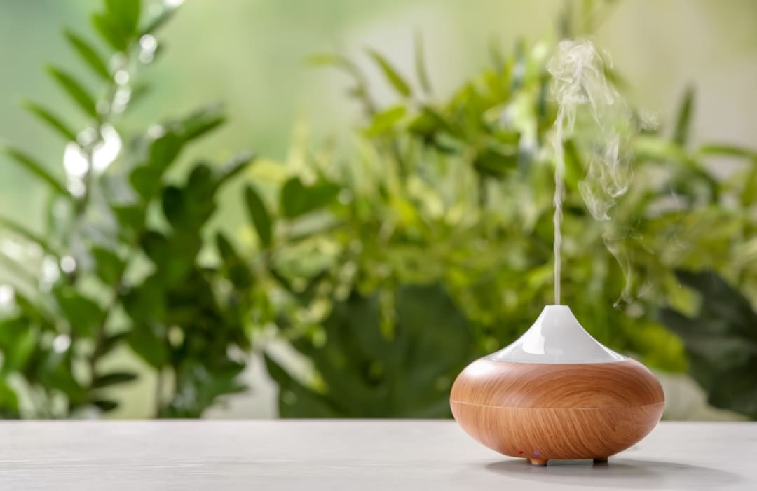 An essential oil diffuser releasing a plume of vapor beside fresh green herbs