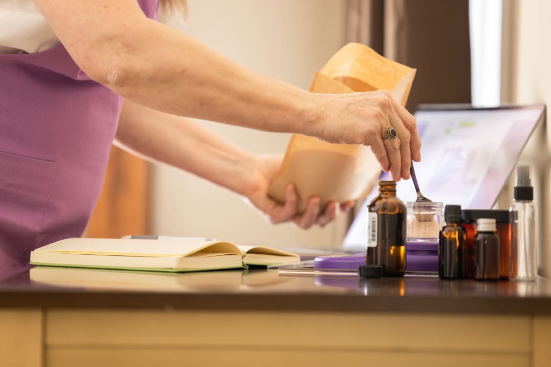 Woman reaching for an amber dropper bottle at a desk with an open journal and study materials