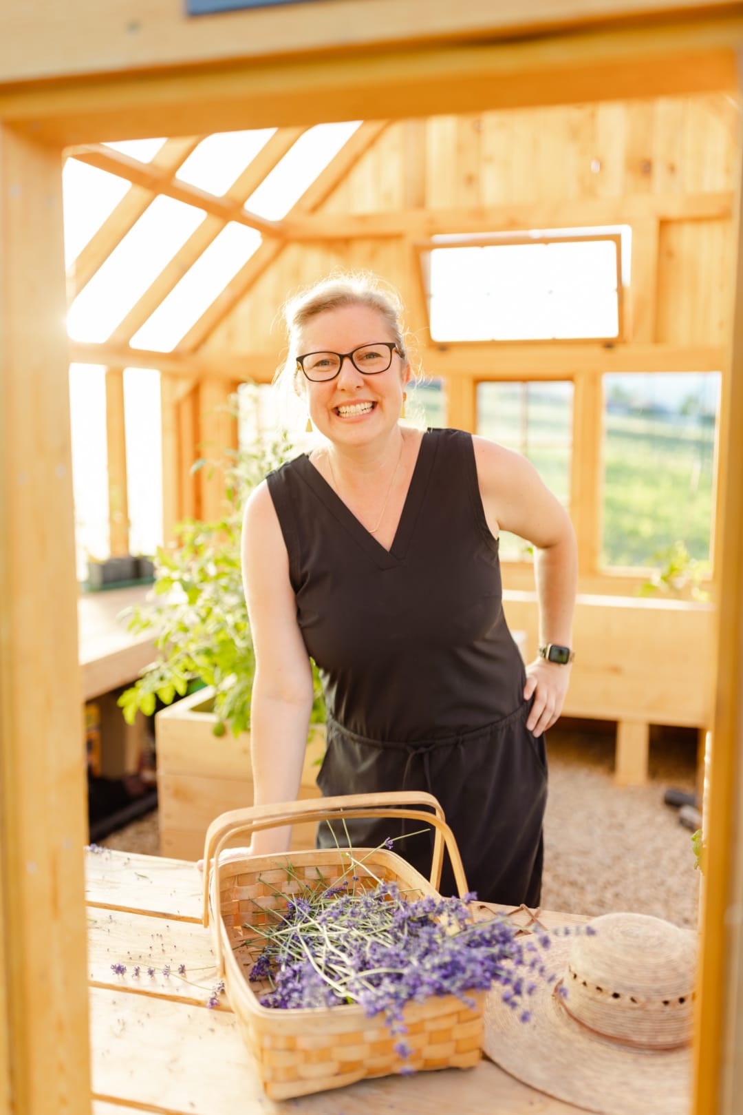 Woman smiling behind a basket of fresh lavender in a sunlit greenhouse