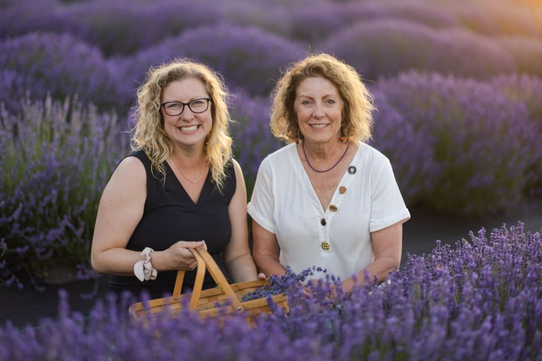 Karen and Jenny Williams holding a basket of fresh lavender in a sunlit lavender field