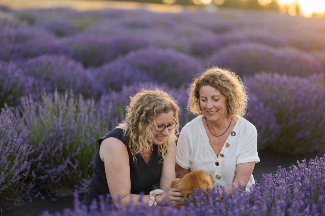 Two women examining lavender blooms together in a field at sunset, smiling