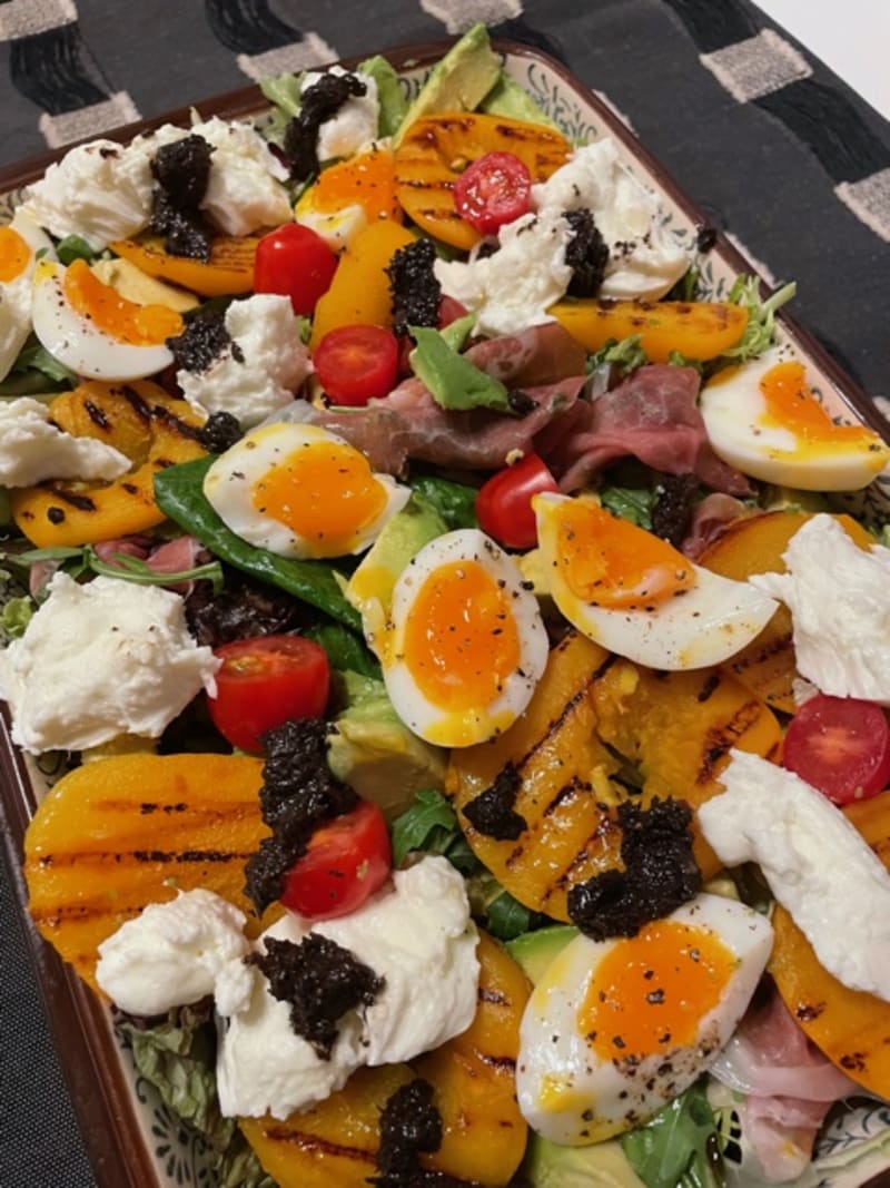 Colorful salad with eggs, mozzarella, grilled peach and prosciutto