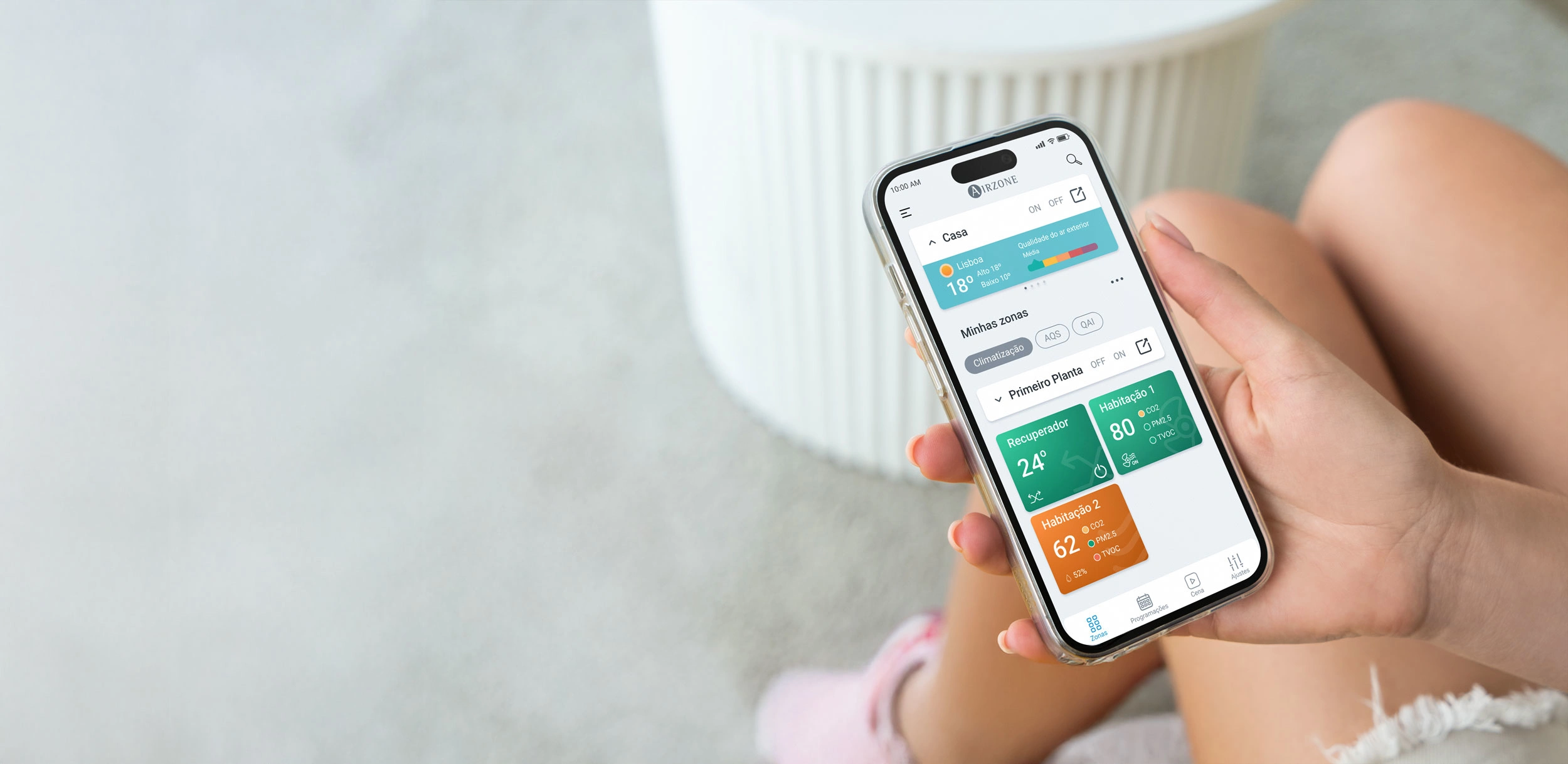 Pessoa segurando um smartphone com a aplicação Airzone Cloud aberta, mostrando o ecrã inicial.
