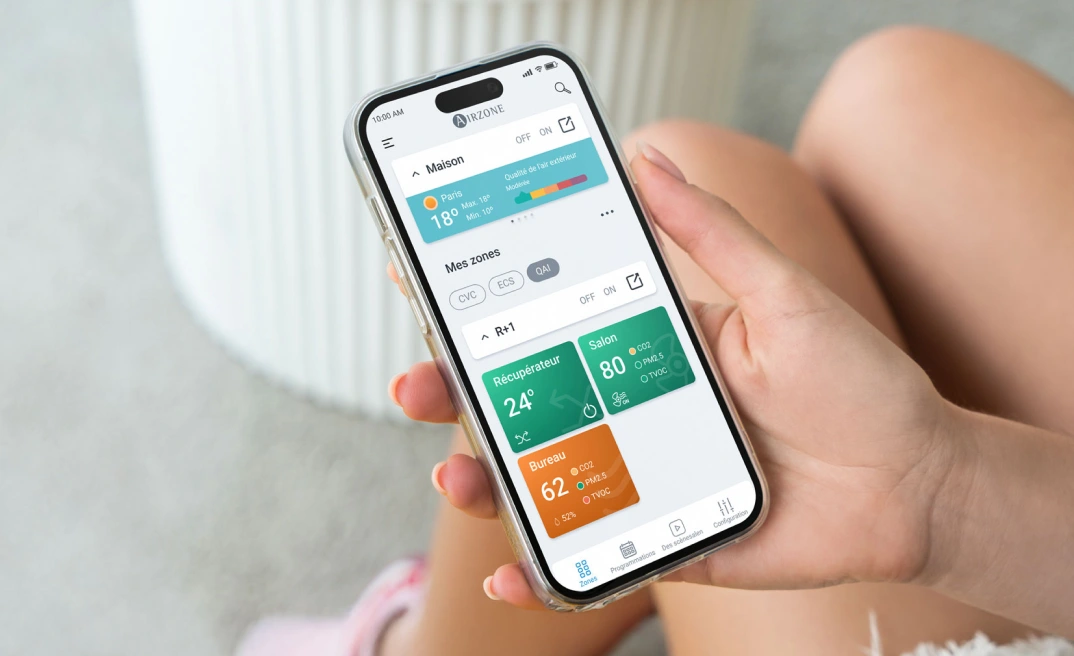 Personne tenant un smartphone avec l’application Airzone Cloud ouverte, affichant l’écran d’accueil.