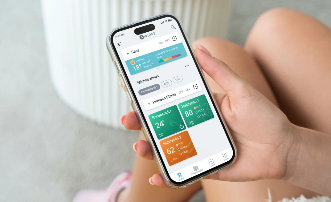 Pessoa segurando um smartphone com a aplicação Airzone Cloud aberta, mostrando o ecrã inicial.